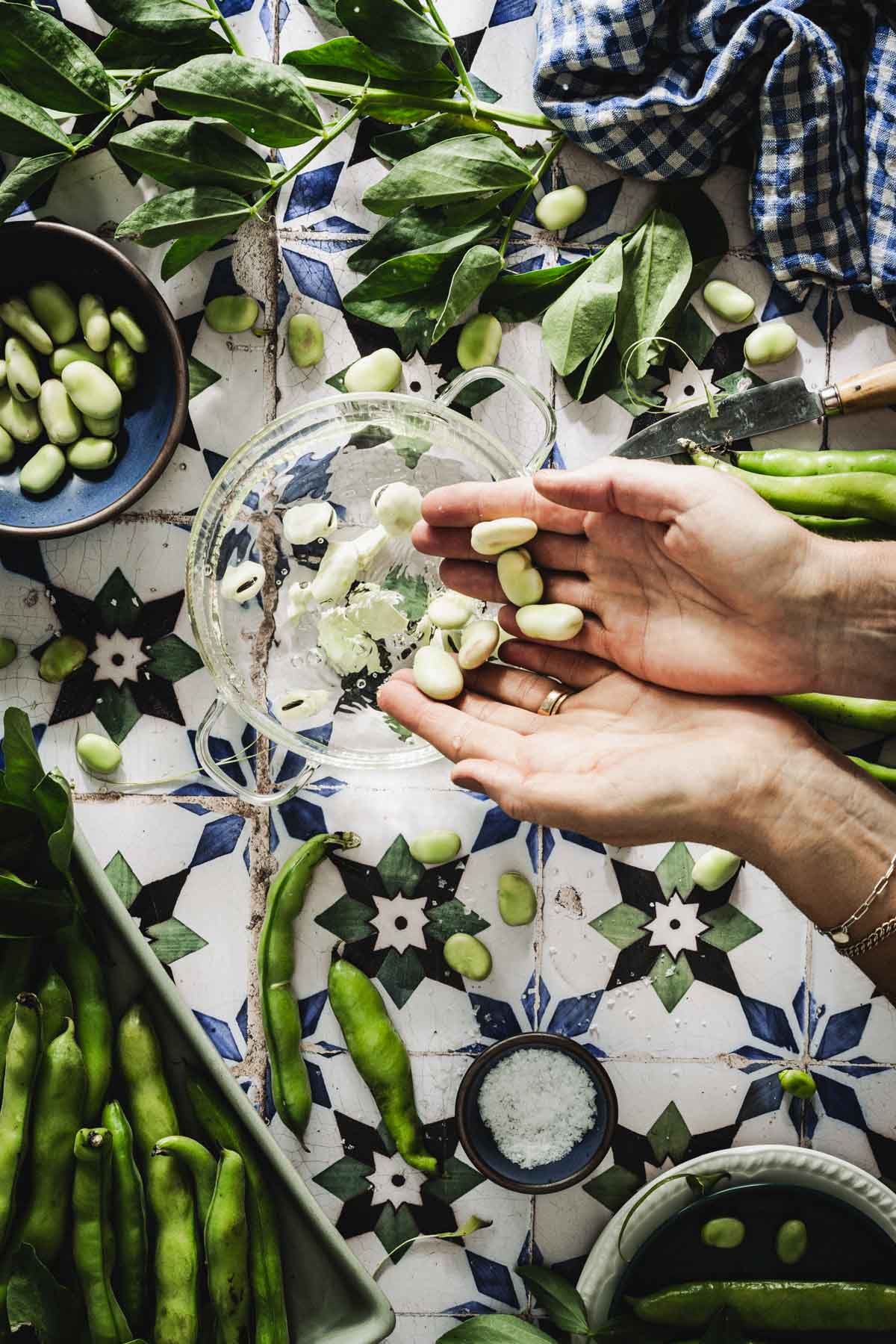 hands in frame dropping fava beans into a pot with water