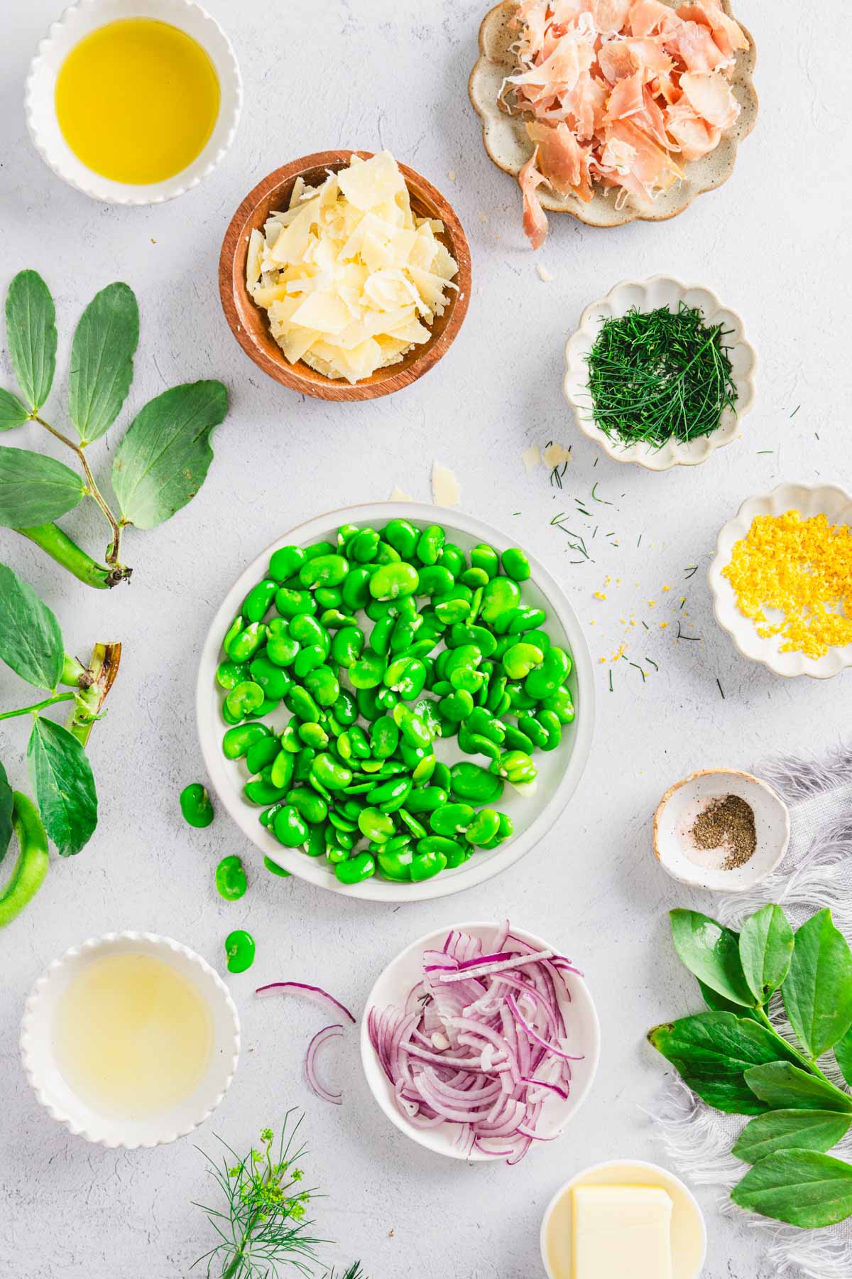 skinned fava beans on a plate, dishes with ingredients to make the salad set around