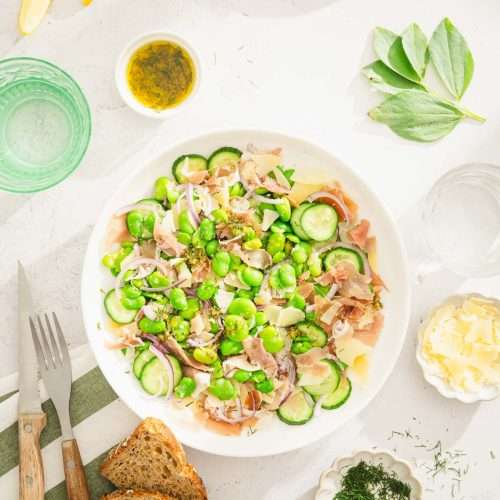 fava bean salad in a serving bowl, glass with water, dish with parm cheese, and dressing, fresh dill, slices of bread