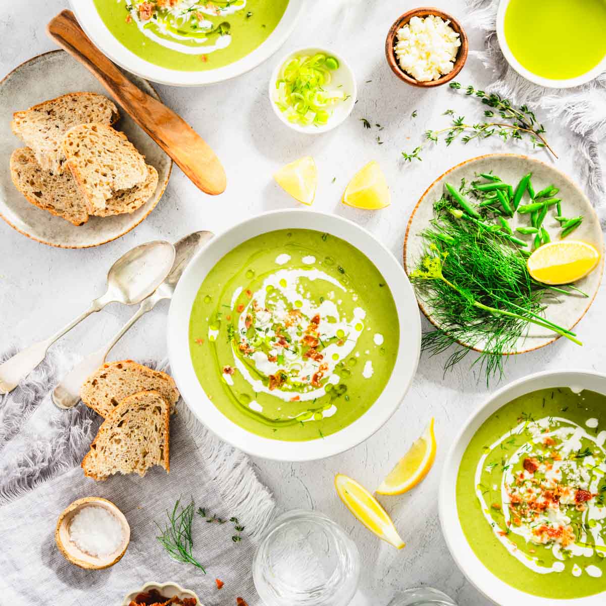 Fava Bean and Leeks Soup in a serving bowls, plate with fresh dill, chives, lemon wedges, feta cheese