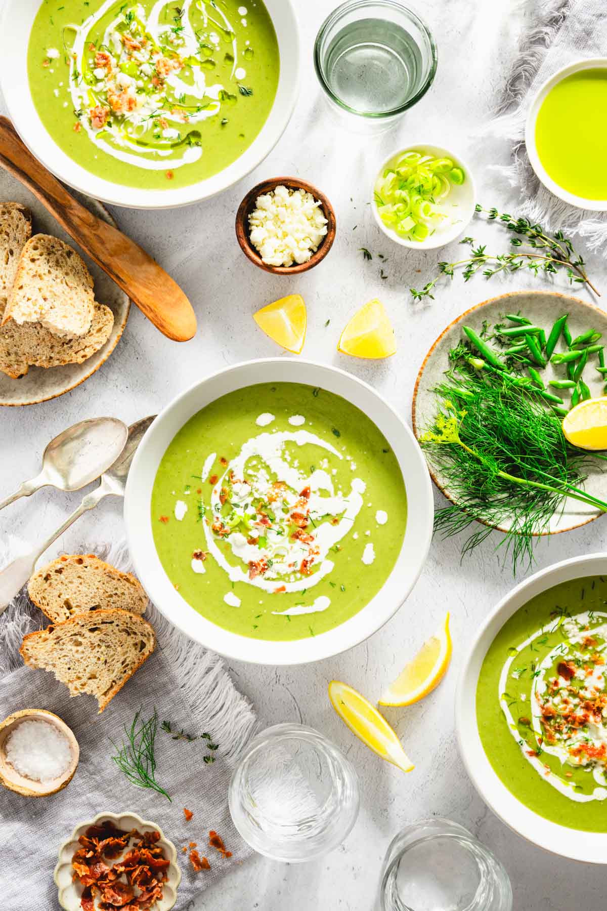 Fava Bean and Leeks Soup in a serving bowls, plate with fresh dill, chives, lemon wedges, feta cheese