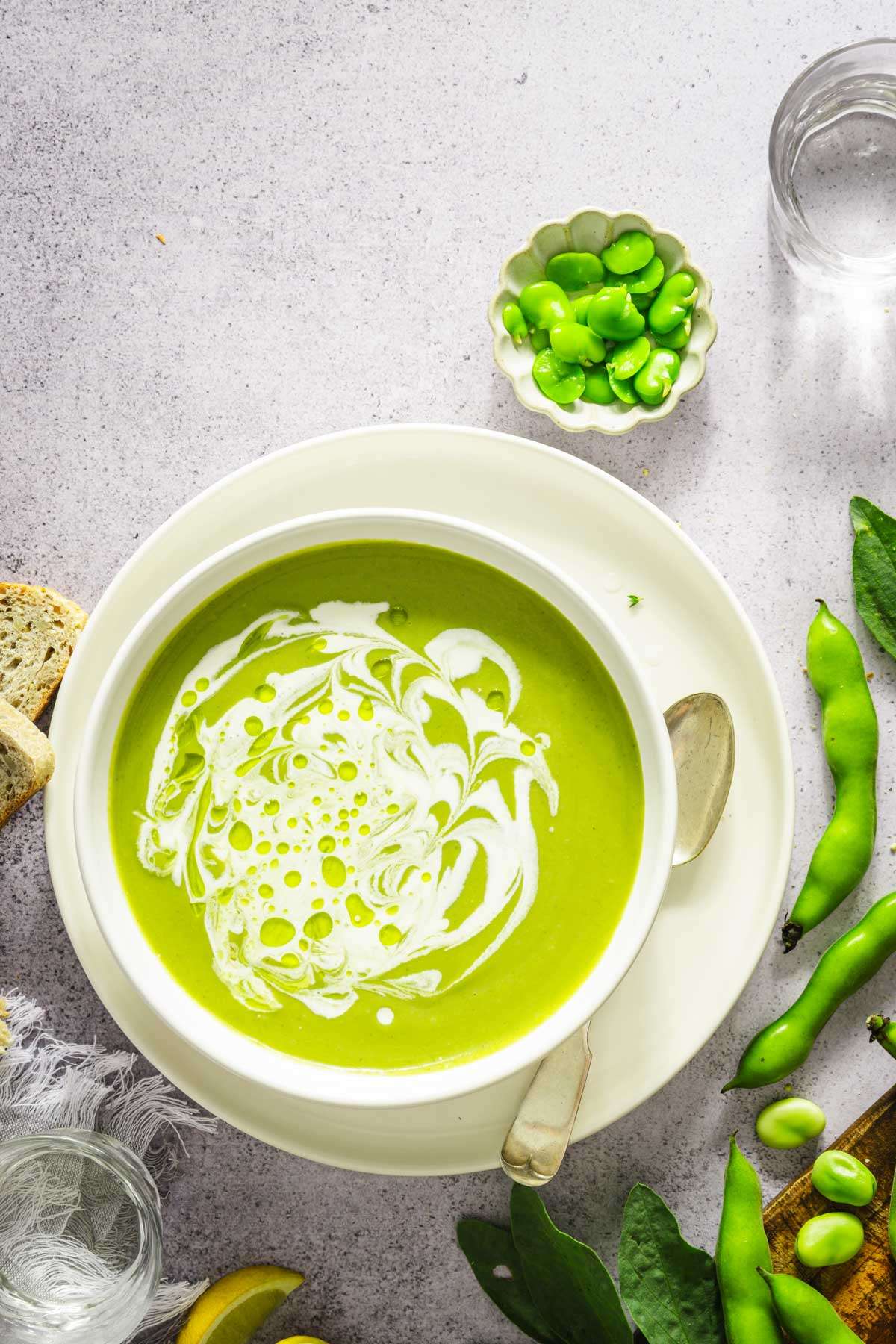 top view of bowl with fava bean soup garnished iwht cream, small dish with fresh favas