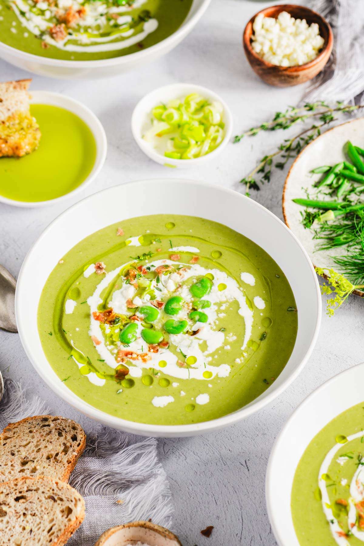 bowl with fava bean soup, garnished with cream, fresh favas and dill oil