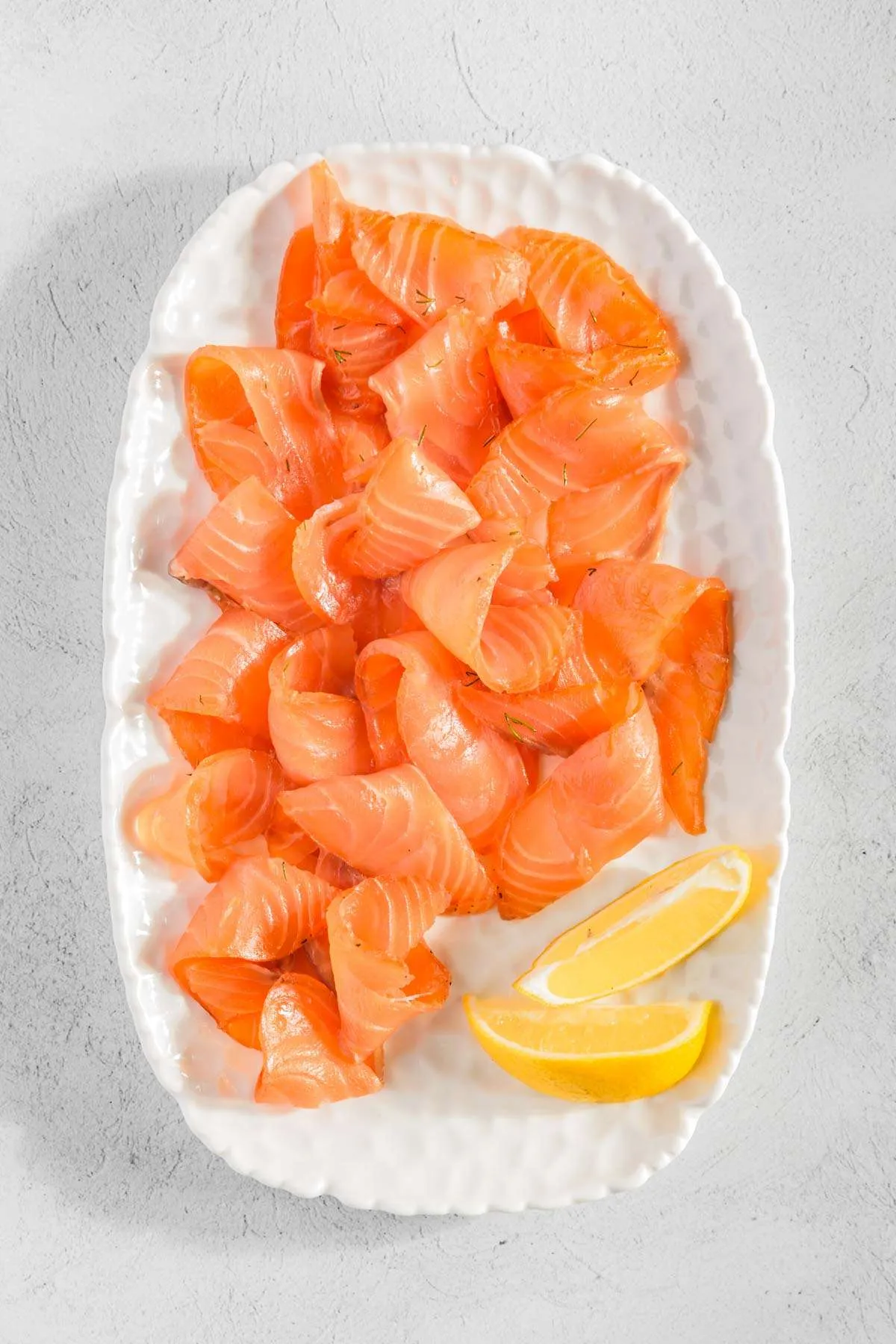sliced gravlax on a serving plate, two lemon wedges
