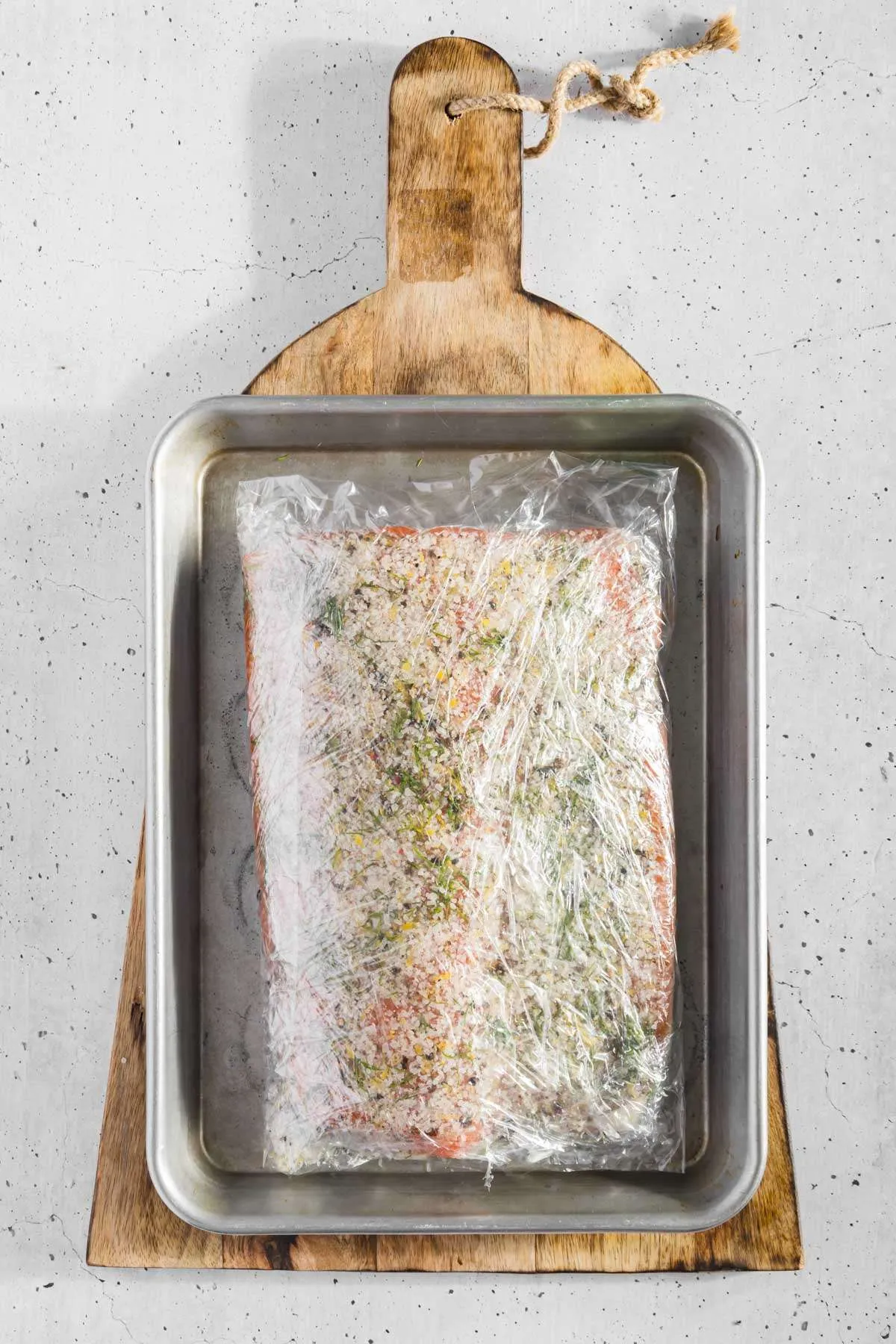 salmon covered in cure wrapped in plastic wrap placed on a baking sheet