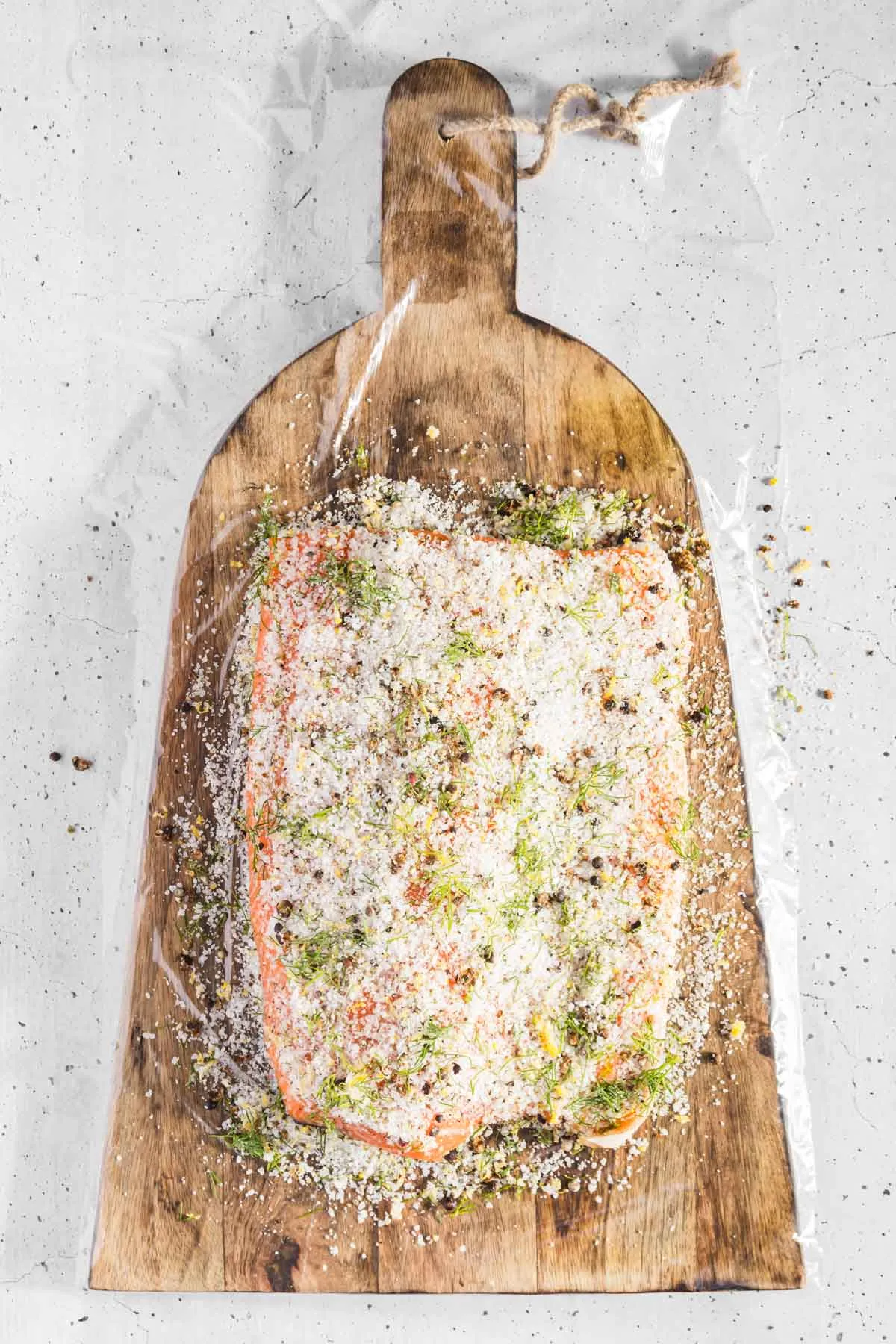 top view of salmon covered with cure, placed on a wooded board and plastic wrap