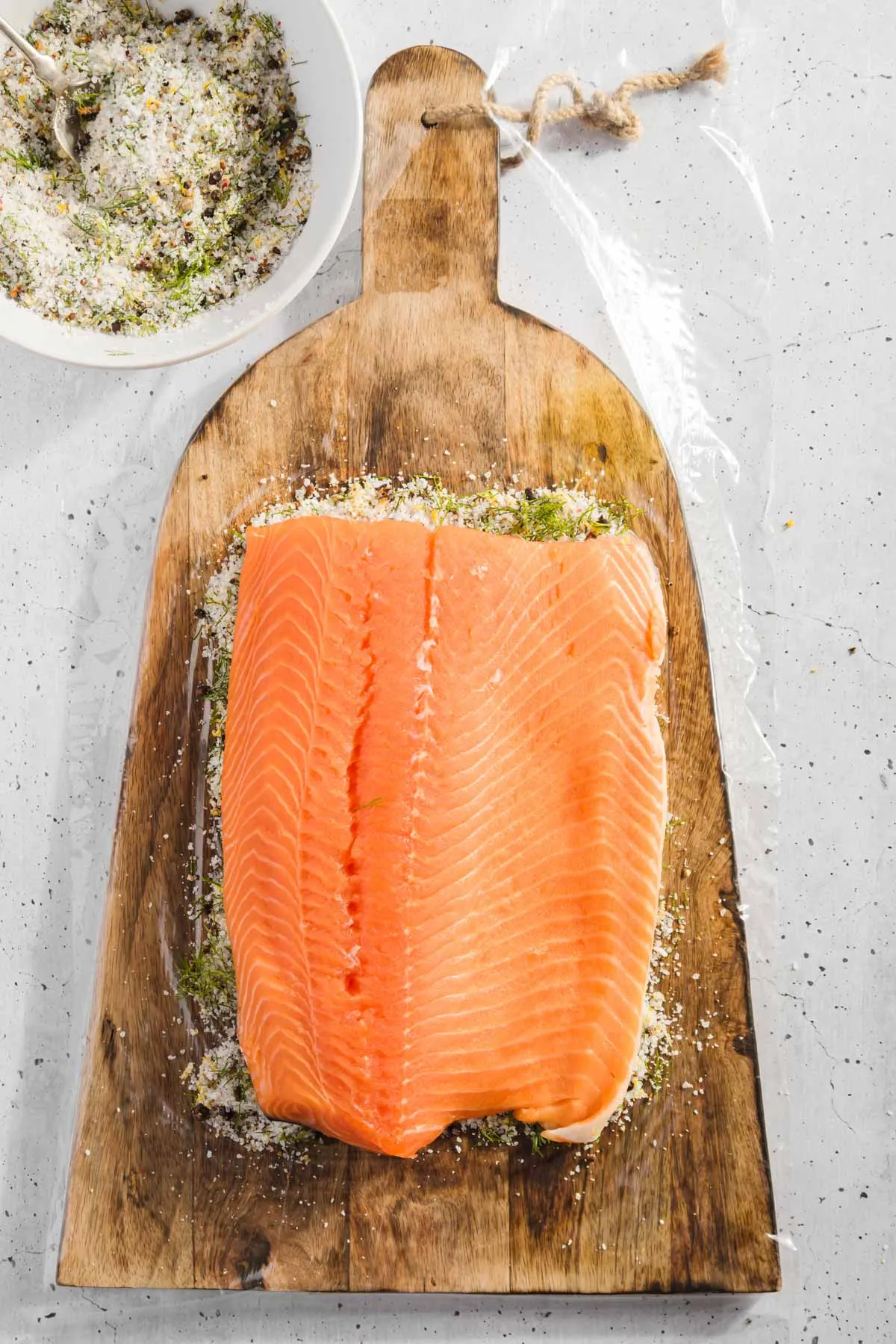 raw salmon on a piece of plastic wrap, with layer of cure underneath it, bowl with cure