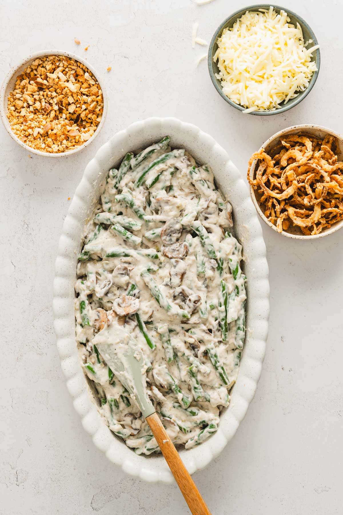 green bean casserole in a deep baking dish, bowl with breadcrumbs, crispy onions and cheese