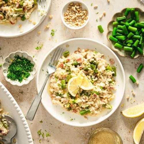 green bean risotto on a serving bowl, dish with green beans, pine nuts, fresh dill, lemon wedges, glasses with wine