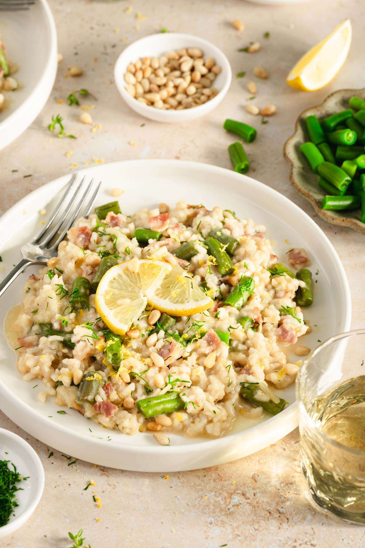 green bean risotto in a serving plate, side of green beans, pine nuts, fresh dill, glass of wine