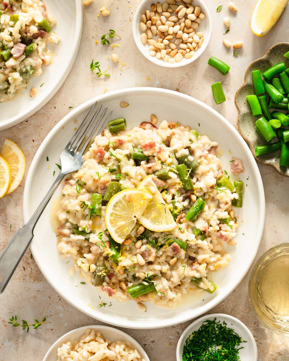 top view of green bean risotto on a serving plate, side of green beans, pine nuts, fresh dill