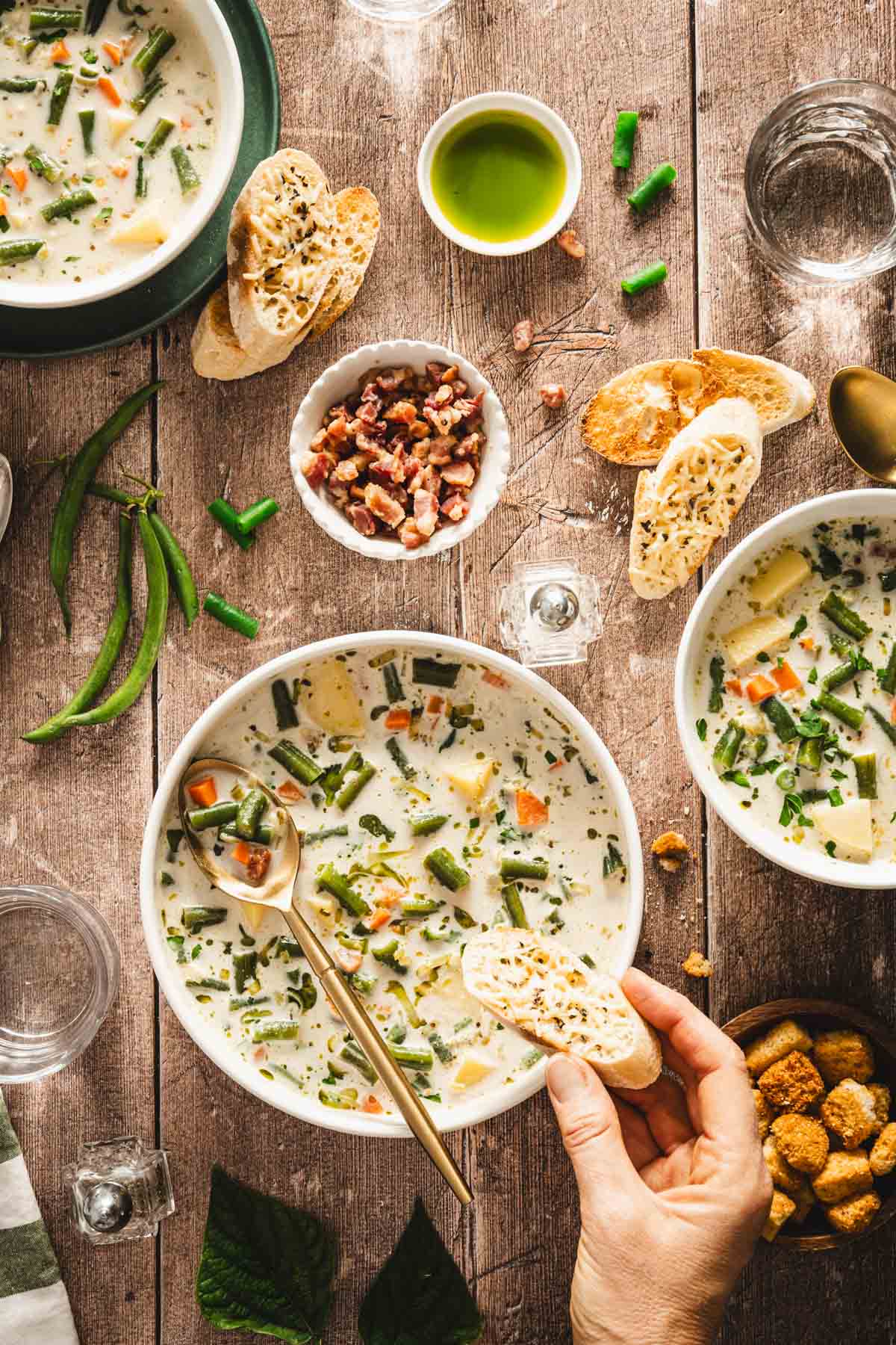 hand in frame holding piece of bread over bowl with green bean soup