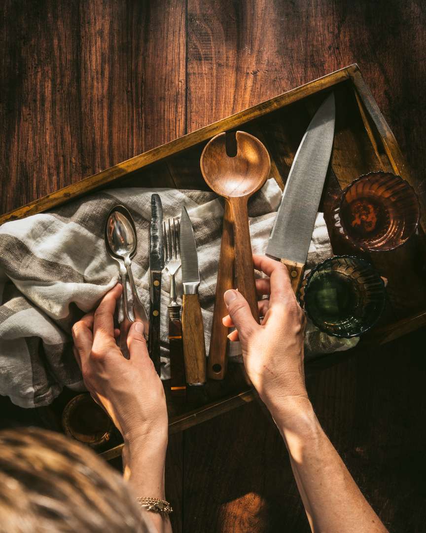 top view at a wooden backdrop, wooden tray and few spoons, knife, wooden spoon and two glasses.