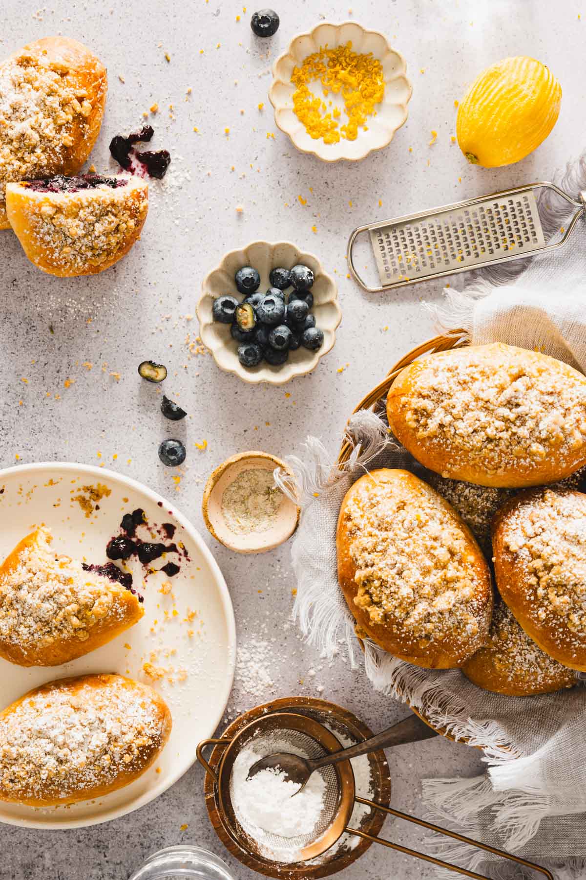 jagodzianki in a basket, few on a serving plate, dish with powdered sugar, fresh blueberries and lemon zest