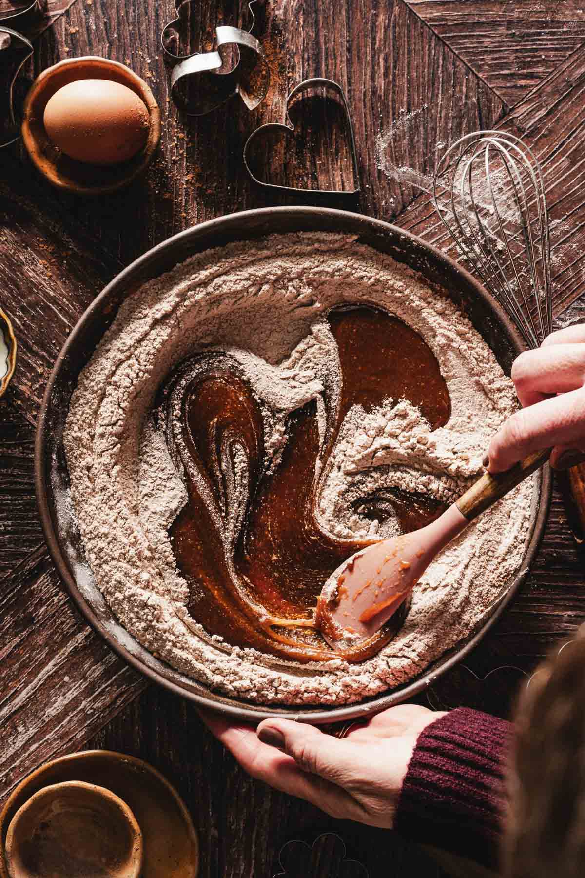 hands in frame stirring the the honey mixture into tohe flour