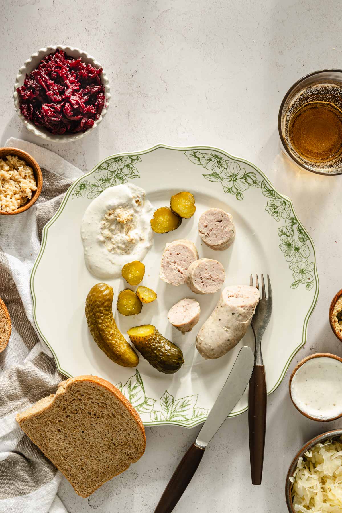 biala kielbasa on a serving plate, pickles, beets, mustard, glass with water, slice of bread around