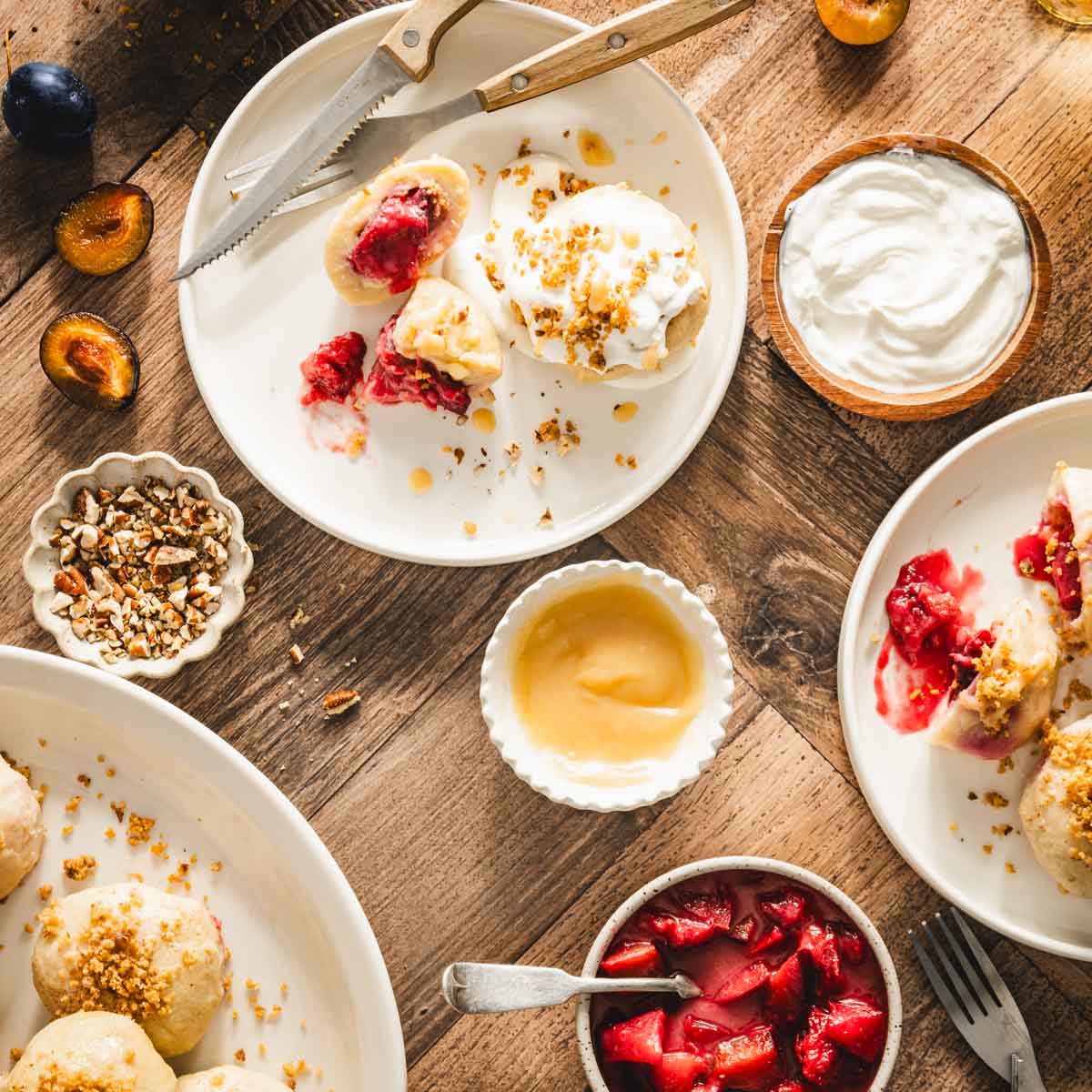 knedle on a serving plates, dish with breadcrumbs, cream, cooked plums, brown butter