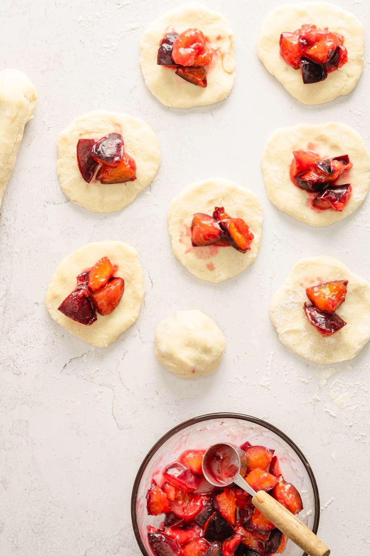 dough formed into circles, bowl with cooked plums, plum filling applied on top of the dough circles