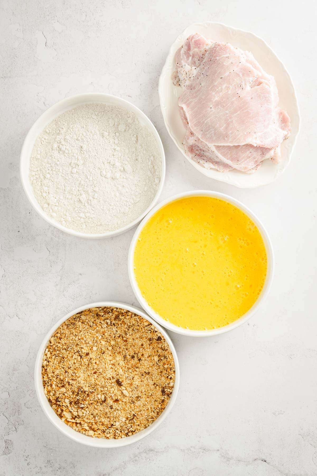 3 bowls, one with egg, one with flour, one with breadcrumbs plate with pork chops