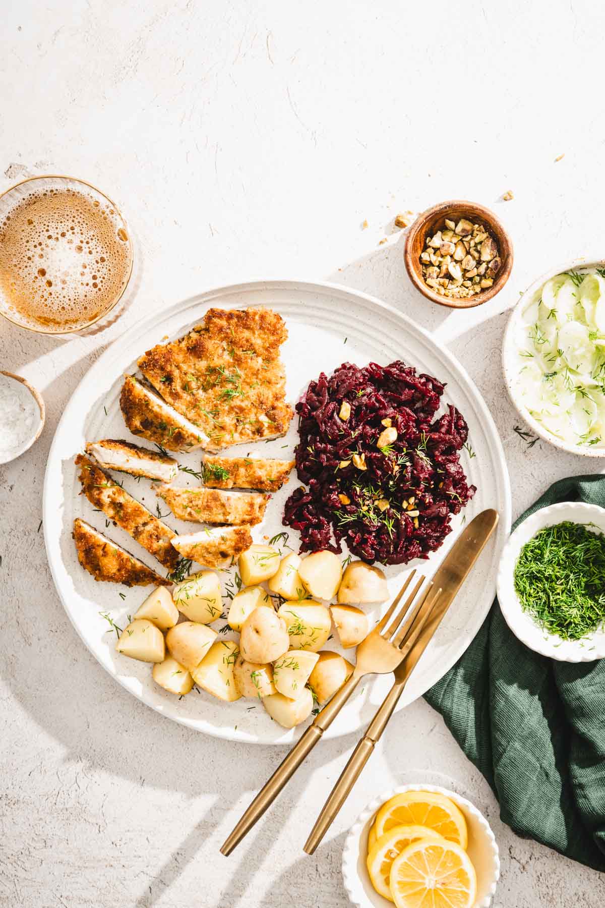 sliced pork chop on a plate with potatoes, beet salad, cucumber salad and fresh dill