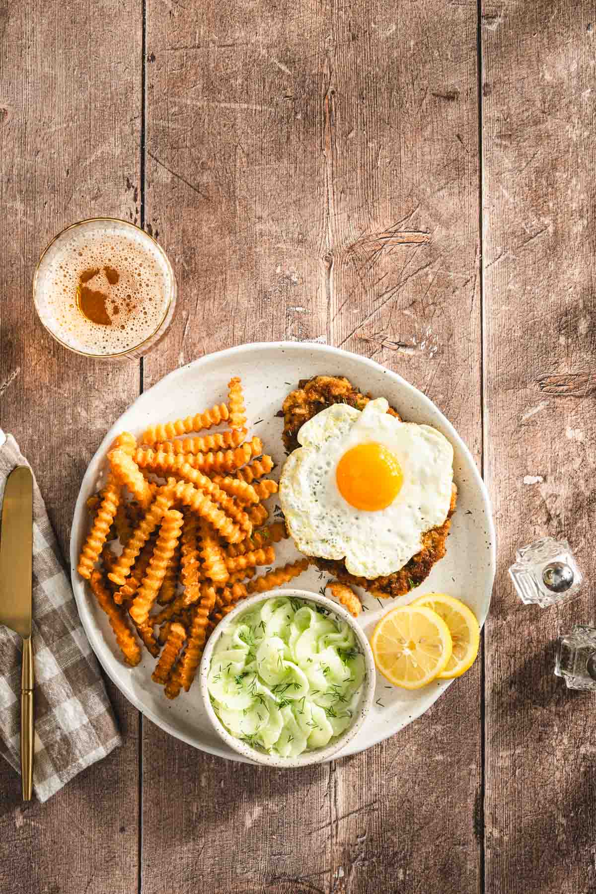 pork chop on a plate with side of fries, and cucumber salad and sunny side up egg