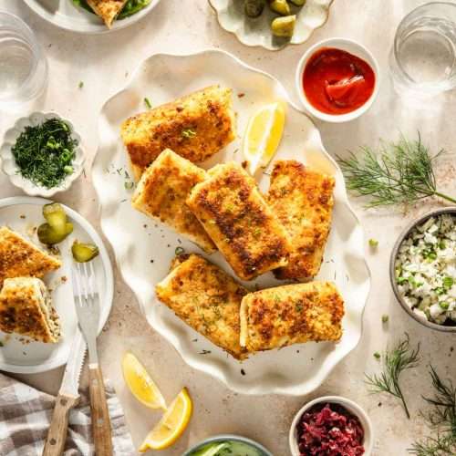 made krokiety arranged on a plate, small dishes with chopped dill, cabbage salad, pickles and other sides