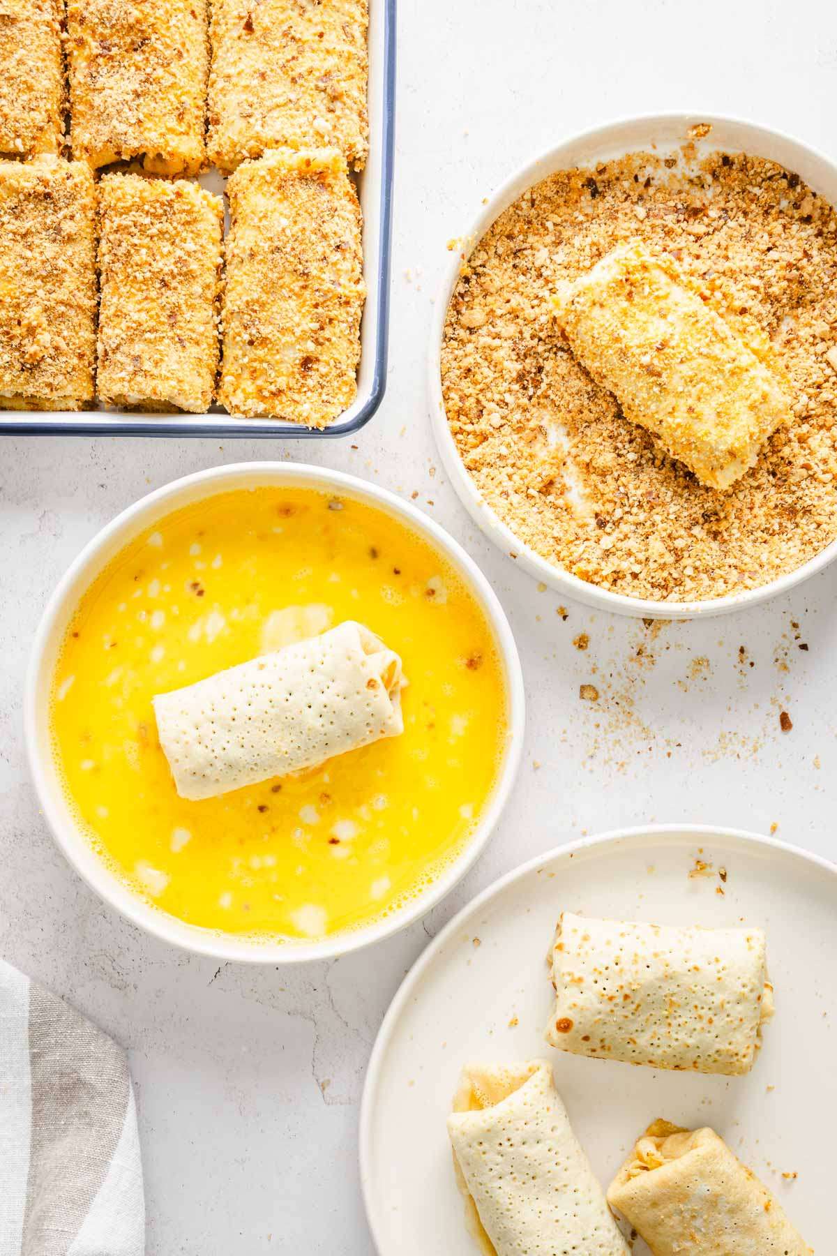 dishes with egg, breadcrumbs and rolled and ready to fry krokiety on a baking tray