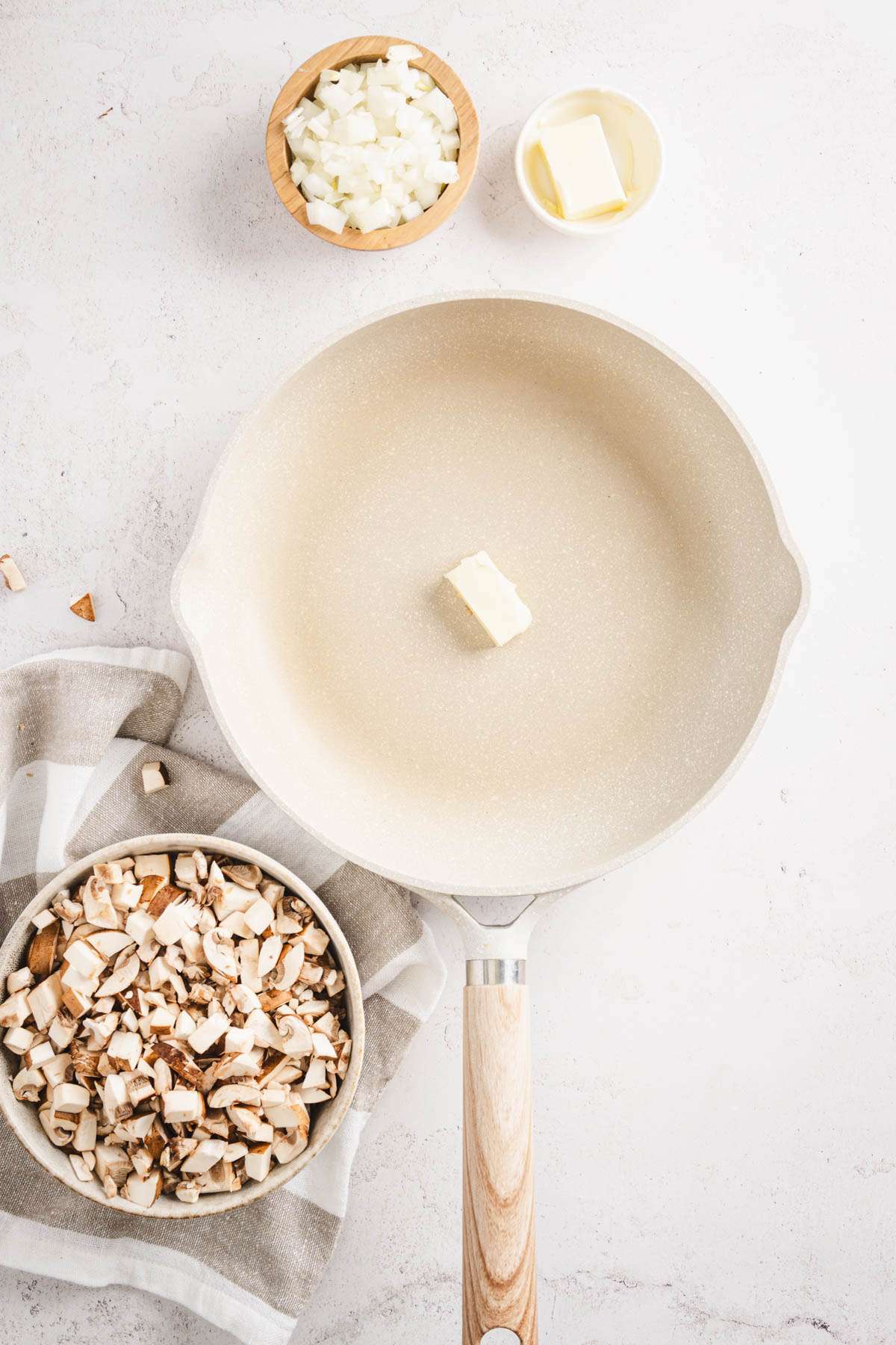 skillet with piece of butter, dish with chopped mushrooms, onions and butter