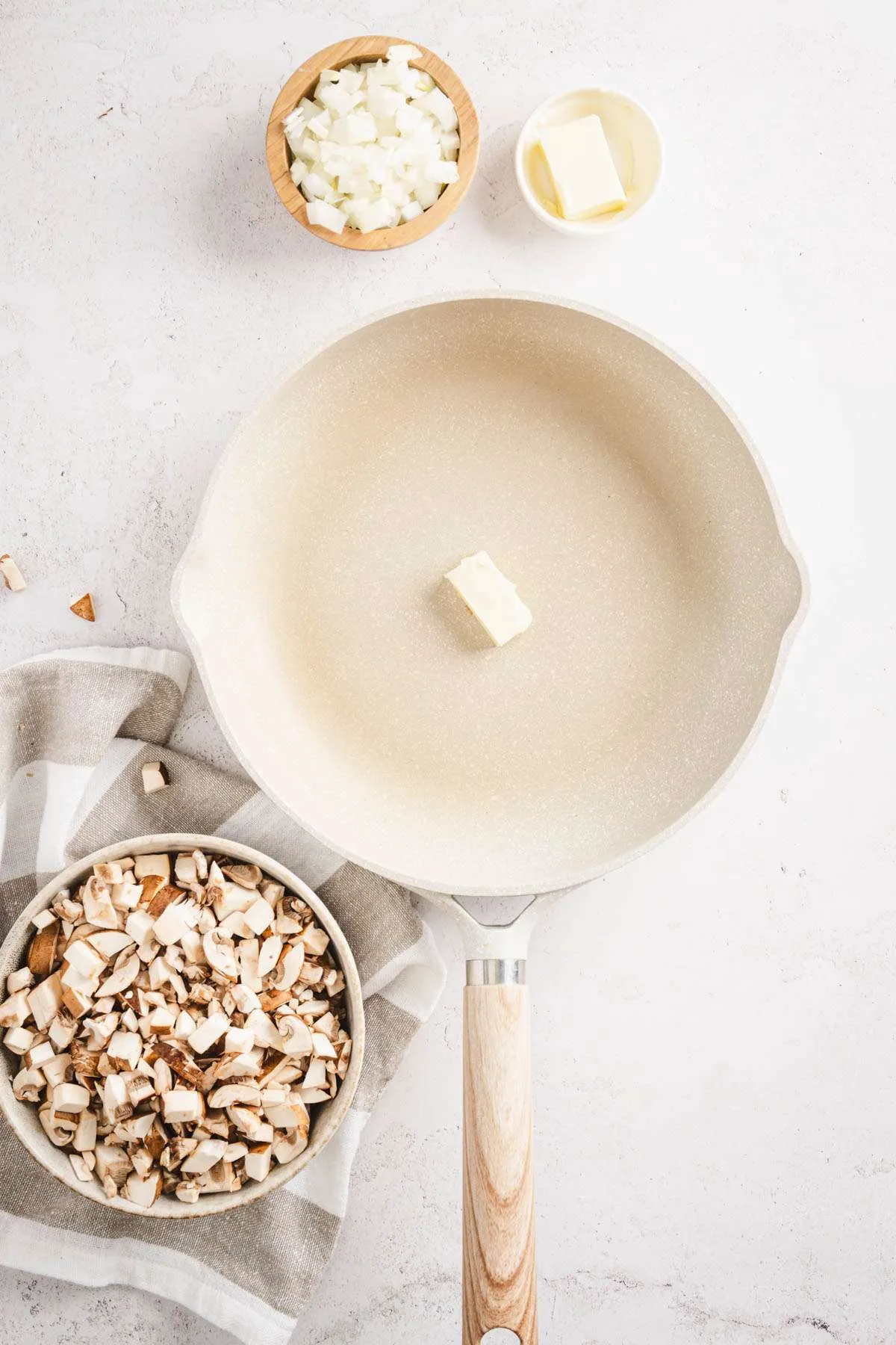 skillet with piece of butter, dish with chopped mushrooms, onions and butter