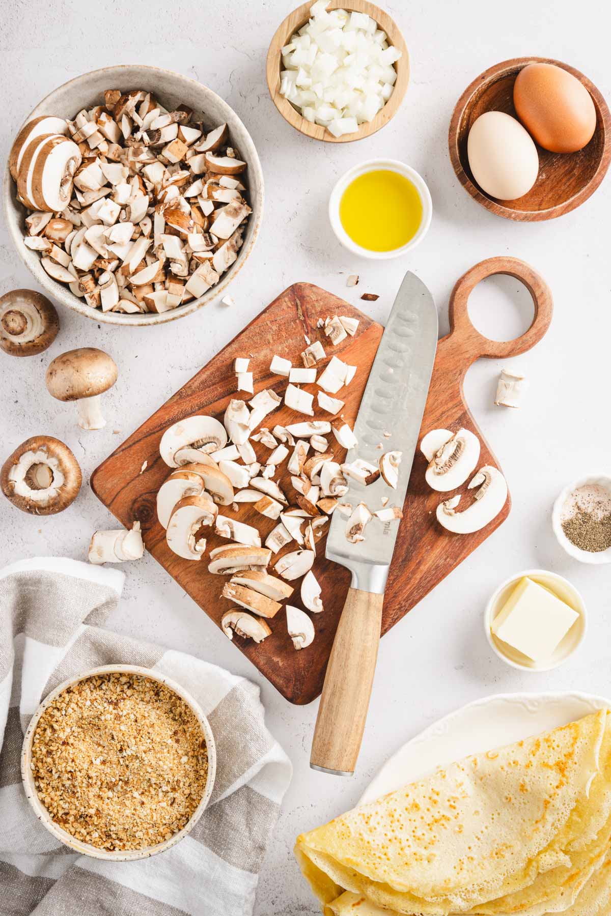 cutting board with mushrooms, knife, dish with kraut, plate with nalesniki