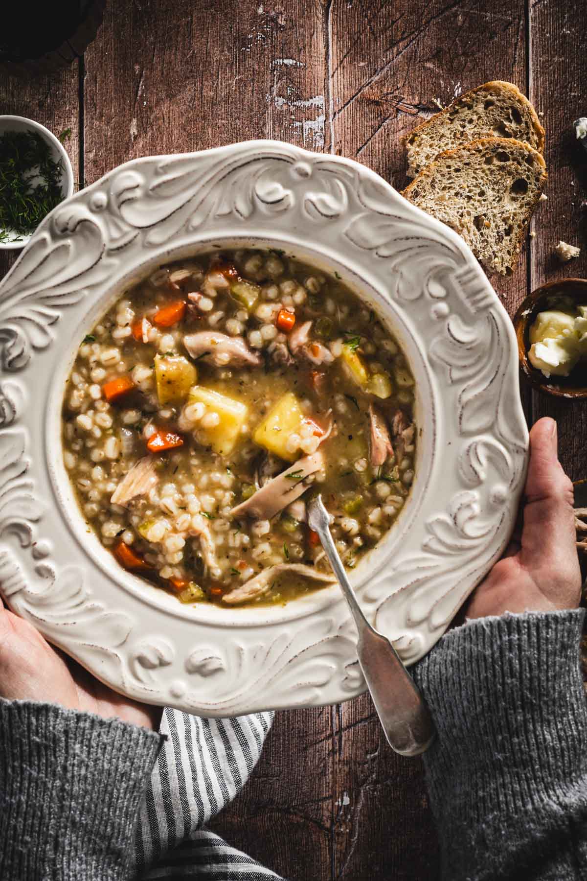 Krupnik in a serving bowls, wooden background, hands in frame holding the plate