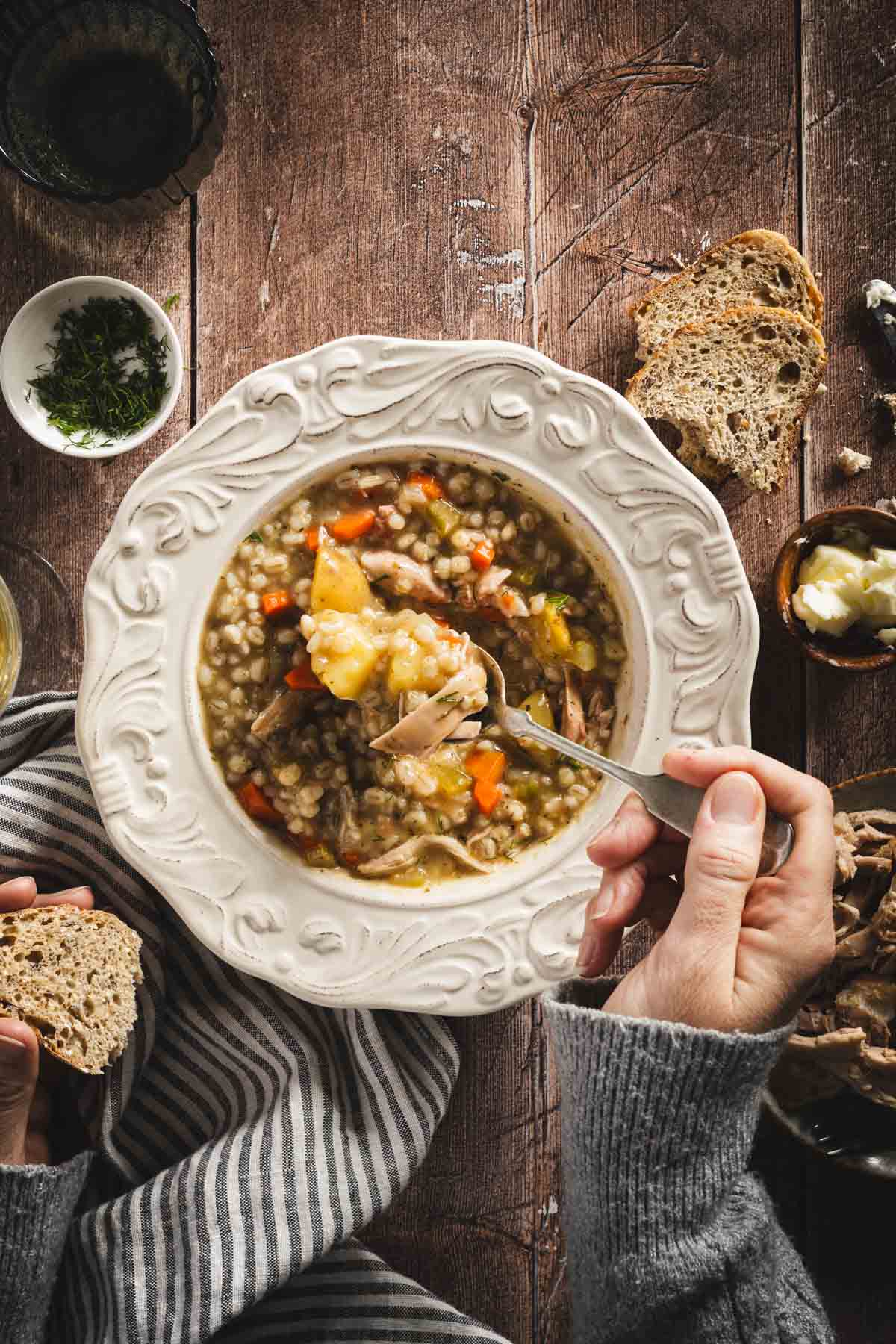 Krupnik in a serving bowls, wooden background, hands in frame holding spoon