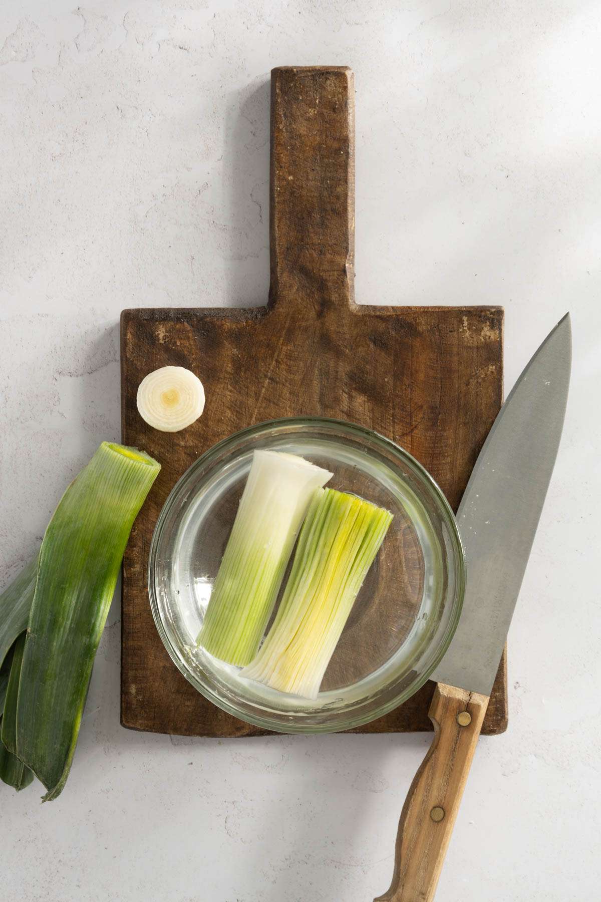 leek o a cutting board, white part cut lengthwise soaking in a bowl with water