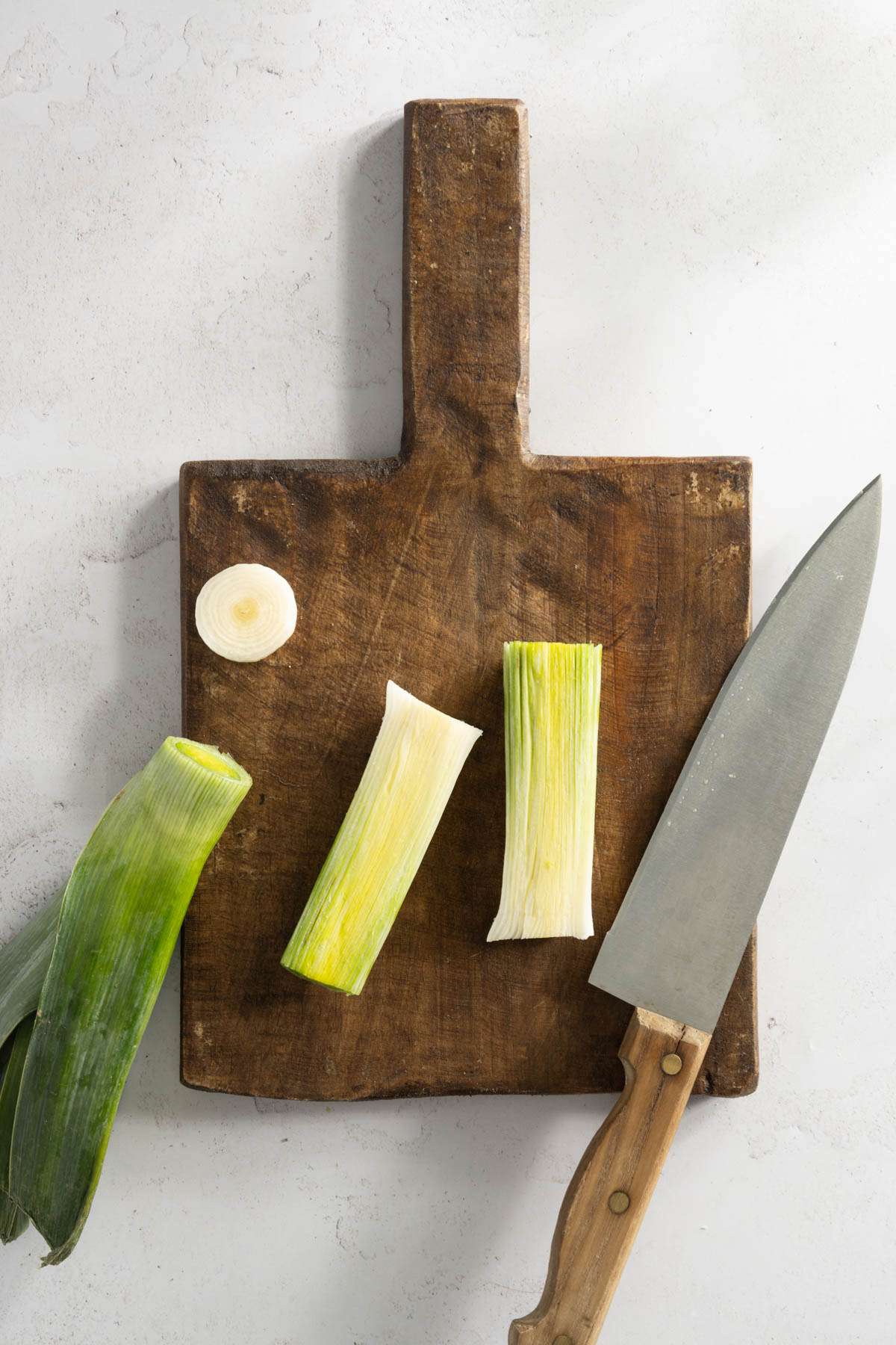 leek o a cutting board, with the end and green part cut off, and the white part cut lengthwise; knife on the side