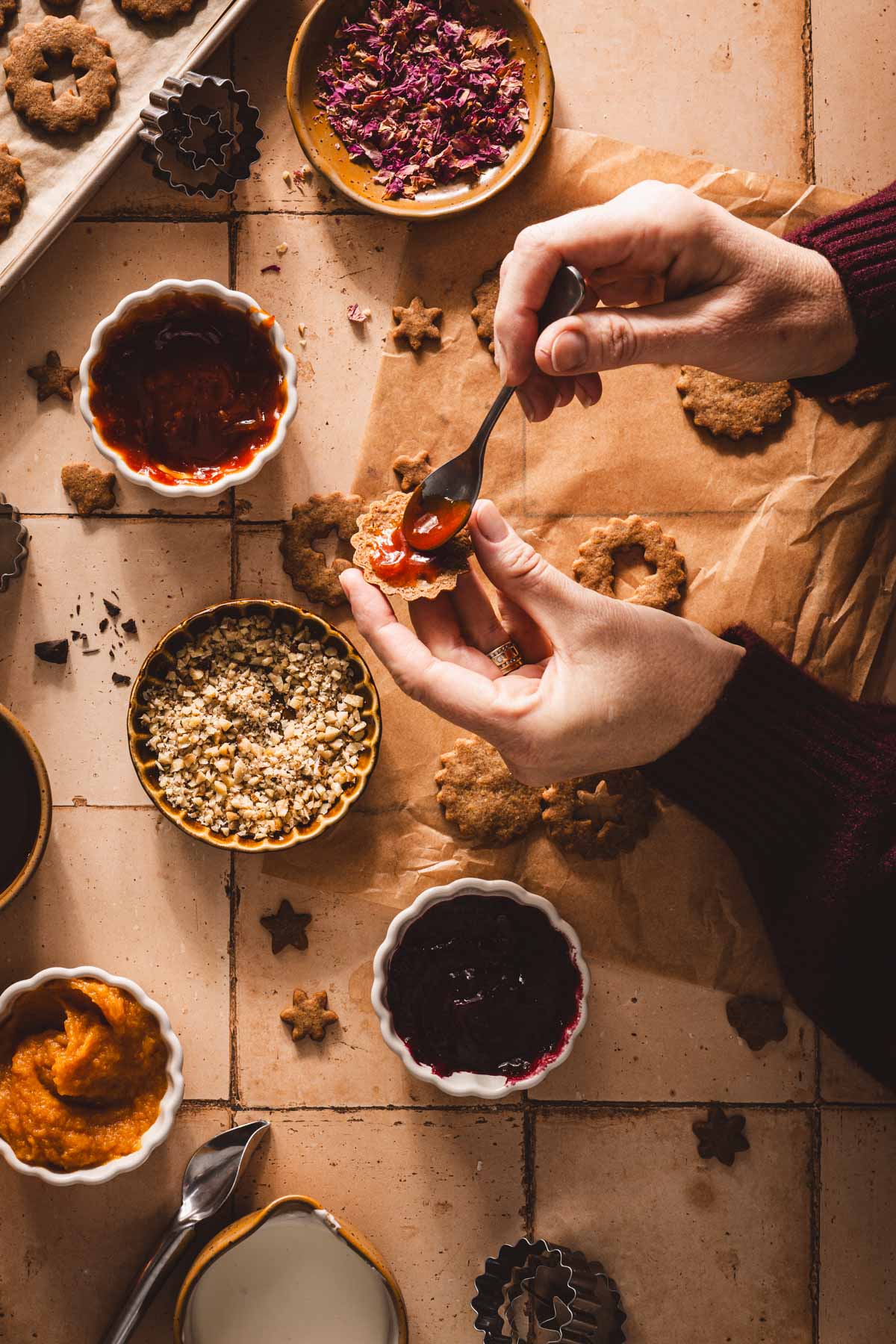 hands in frame adding jam to the bottom cookie