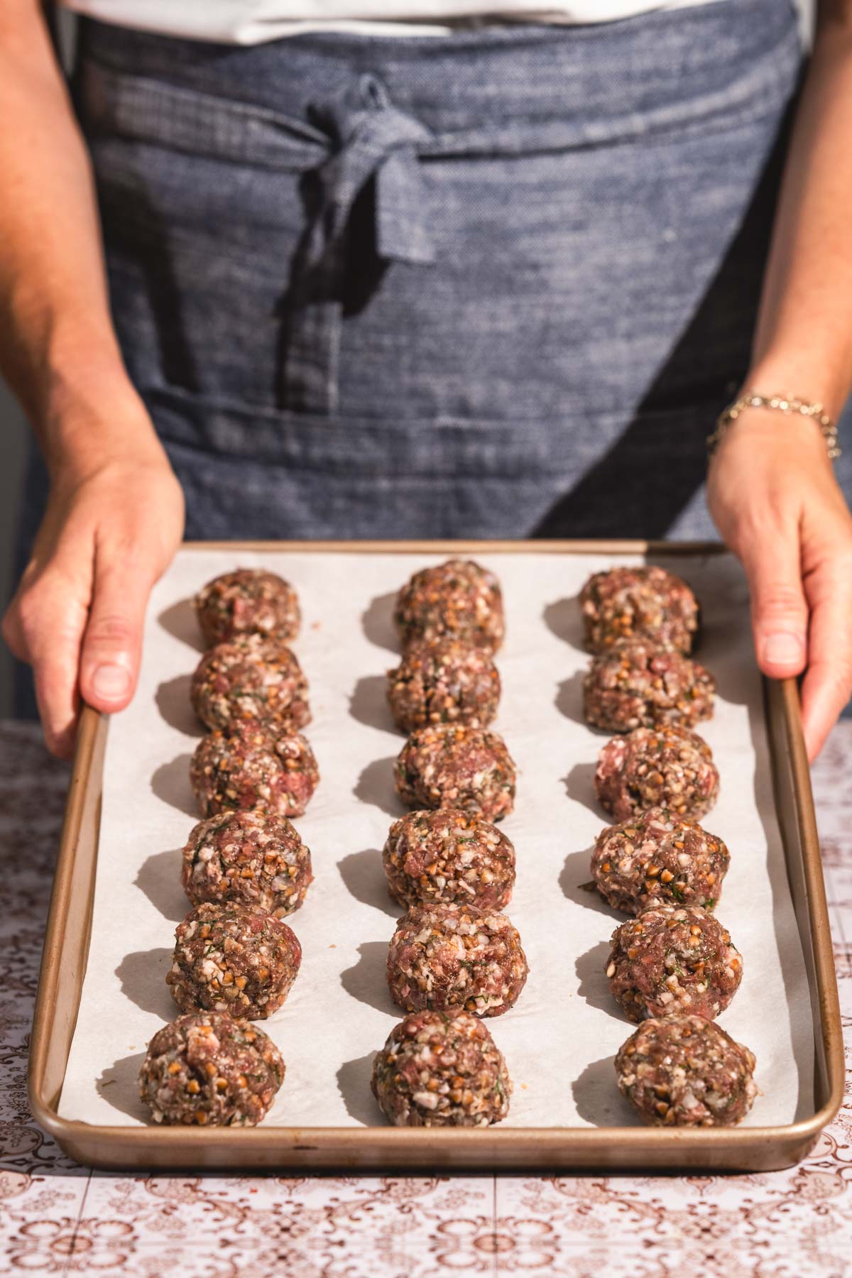 hands in frame holding baking shett with raw meatballs