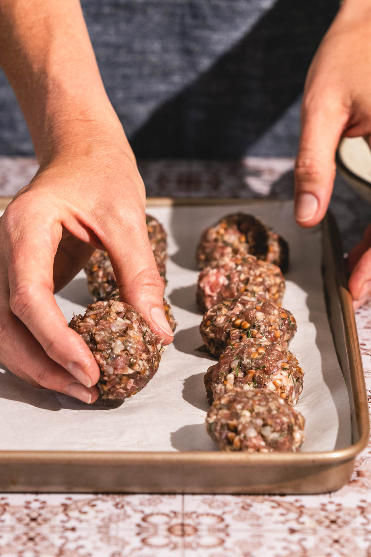hands in frame placing a meatball on a baking sheet