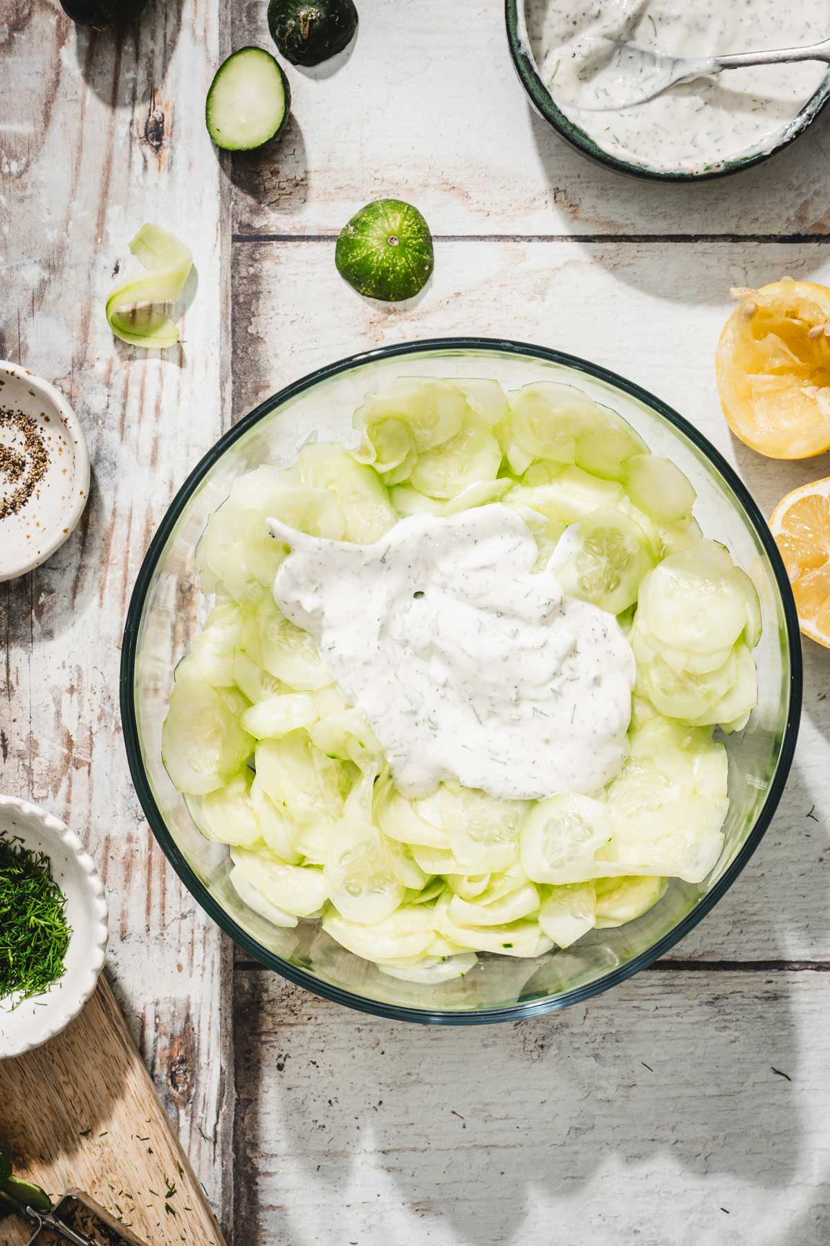 sliced cucumbers added to a glass bowl with a dollop of a dressing