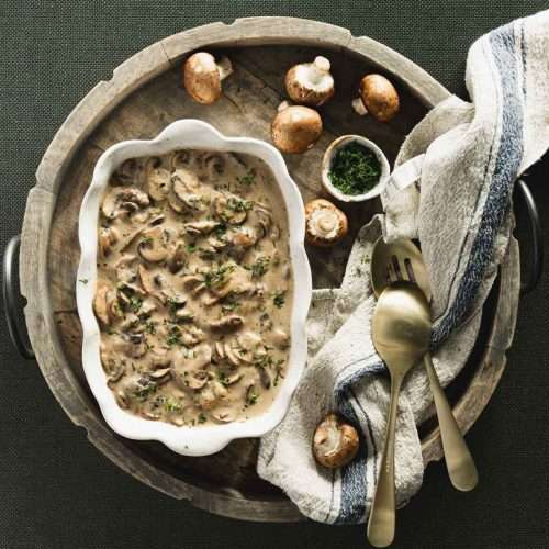 mushroom sauce in a serving dish presented on a carrying wooden tray, few raw mushroom's, utensils, napkin