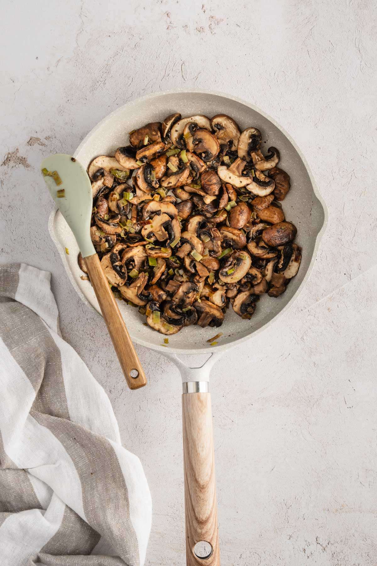 skillet with cooked down mushrooms in it, spatula, napkin