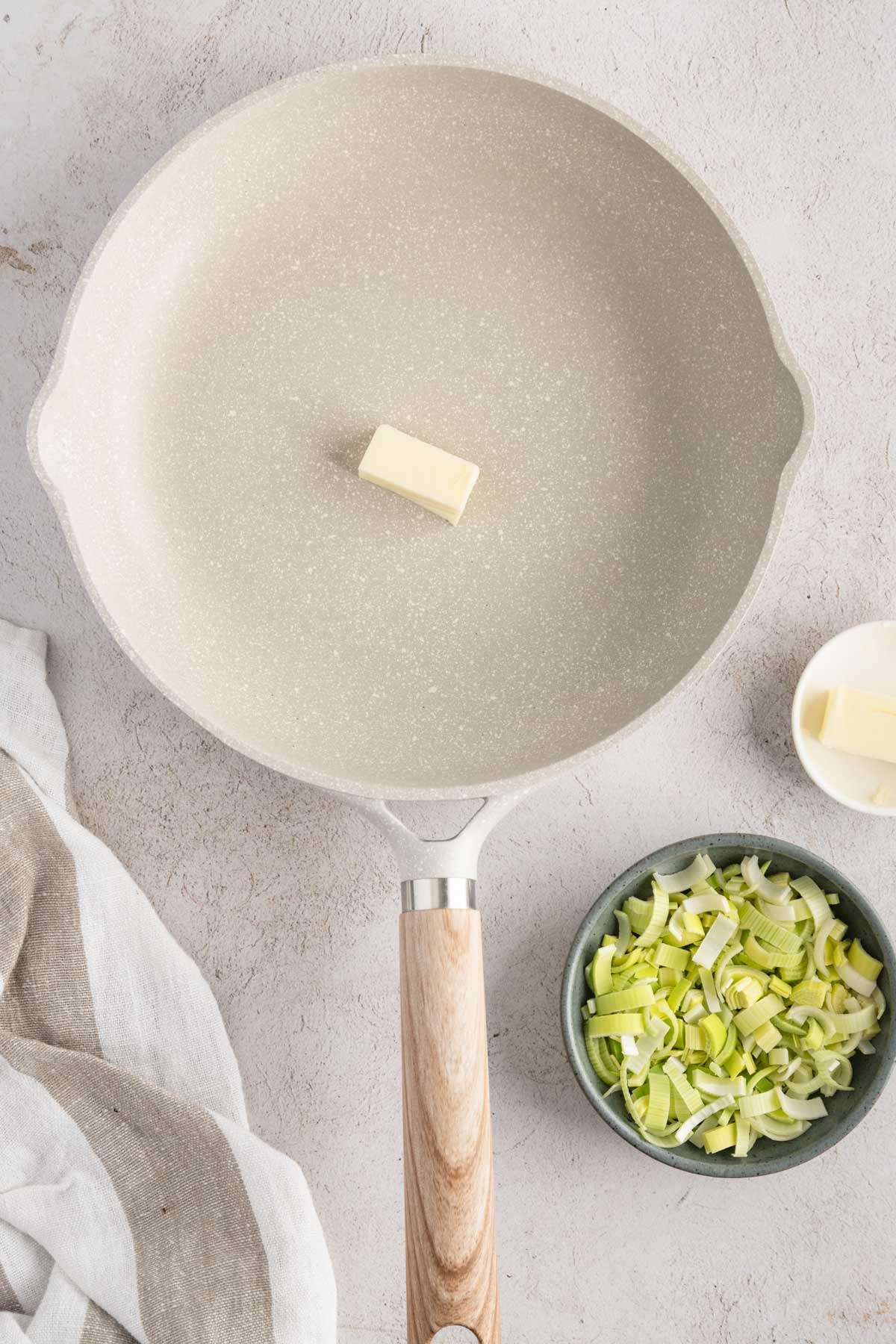 skillet with piece of butter on it, small dish with butter and another one with cut up leeks