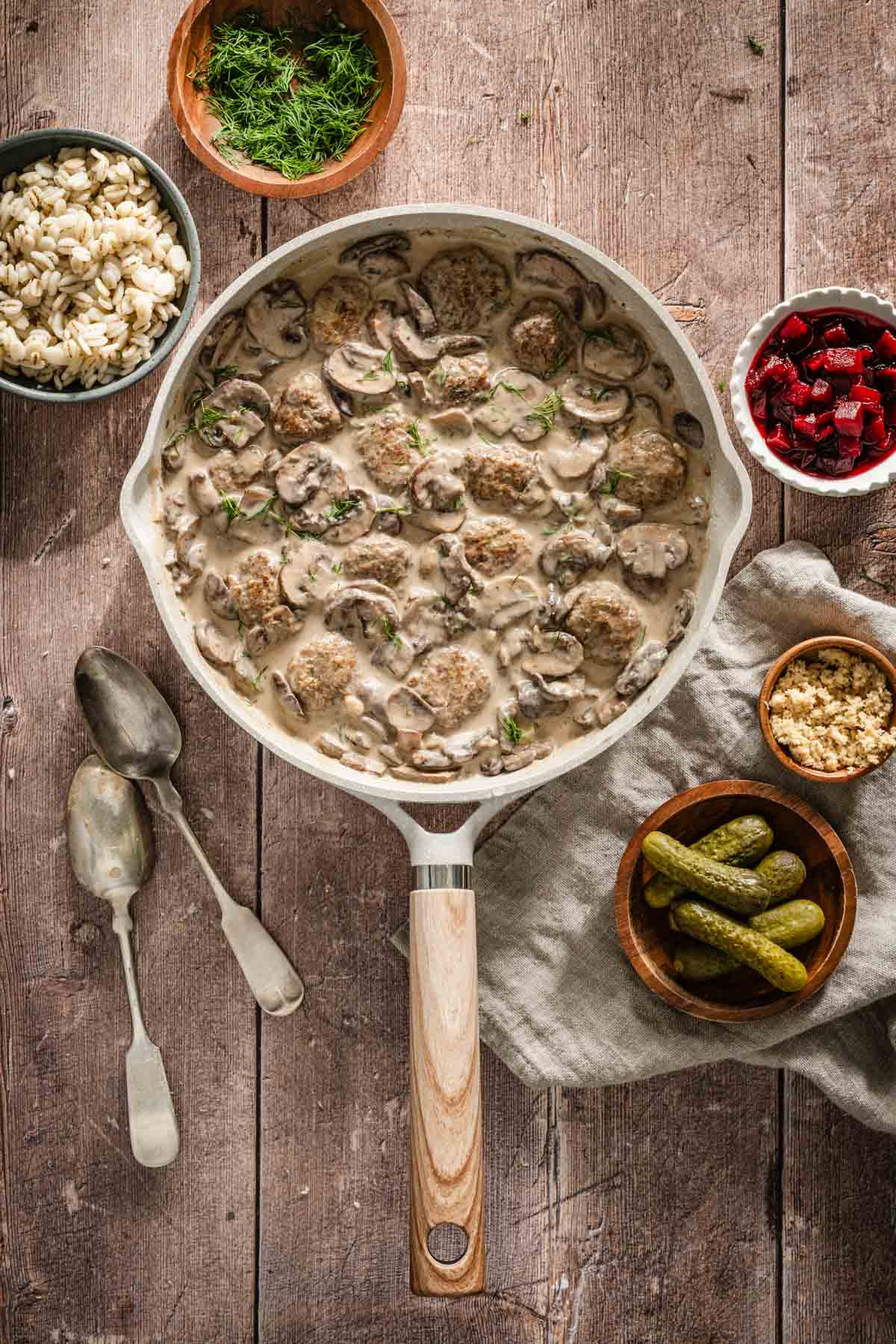 mushroom sauce in a skillet, small dishes with sides, barley, beets, pickles, horseradish, tweo spoons