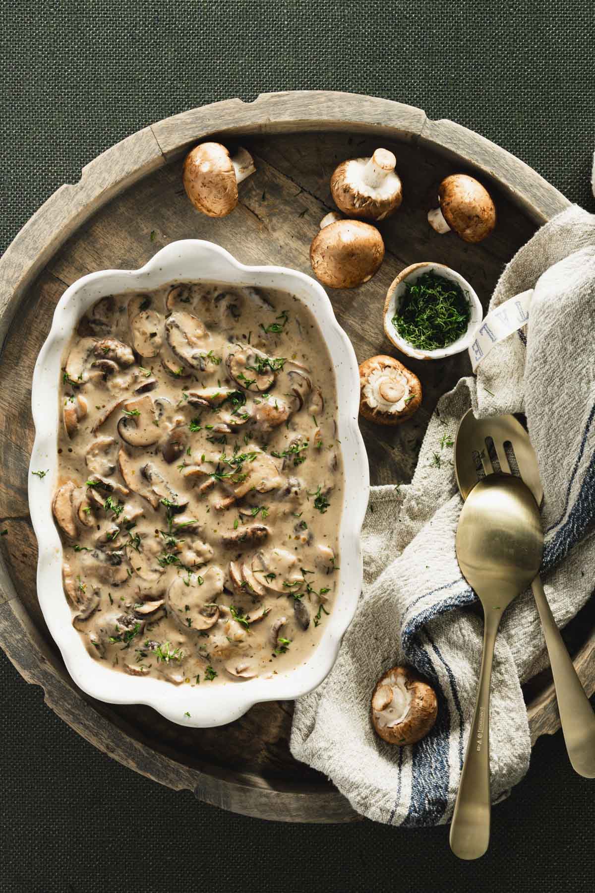 mushroom sauce in a serving dish presented on a carrying wooden tray, few raw mushroom's, utensils, napkin