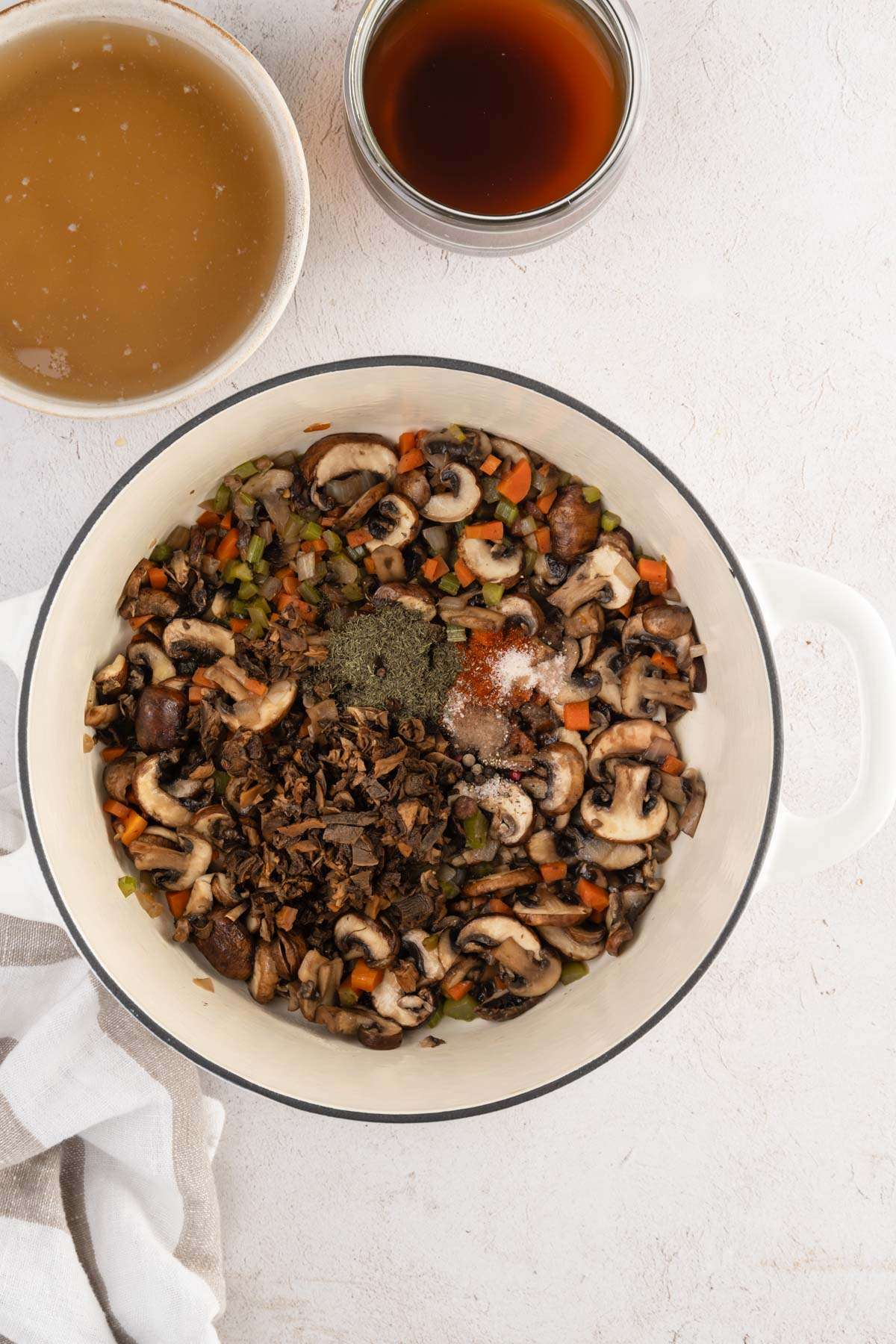 Mushroom and veggies in a cooking pan, bowl with broth and mushroom water, seasonings