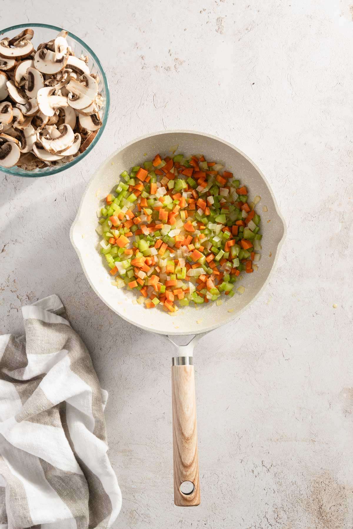 frying pan with cooked chopped carrots, celery and onion; small bowl with sliced mushrooms