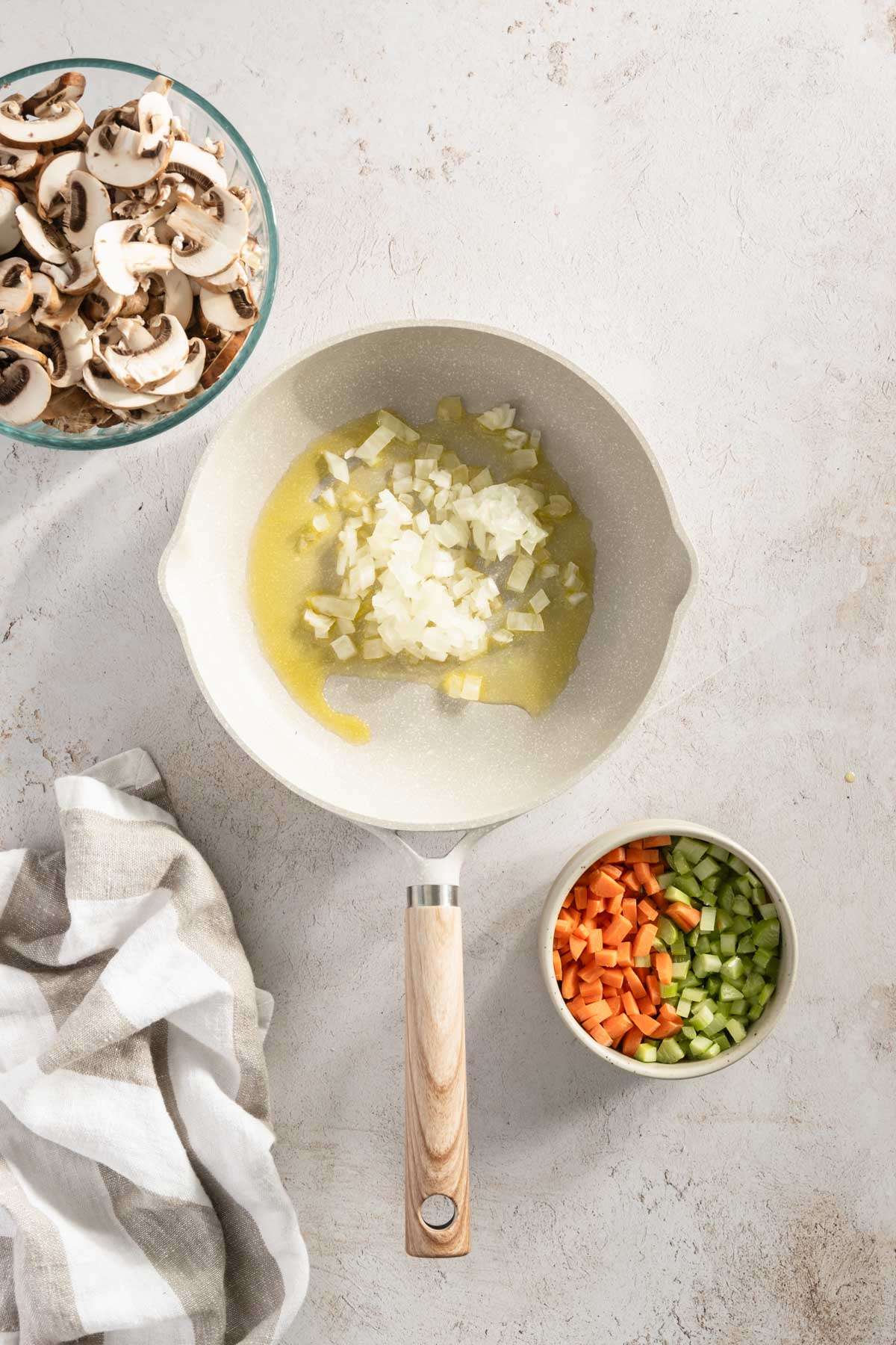 frying pan with drizzle of oil, chopped onions; small bowl with sliced mushrooms and another one with carrots and celery