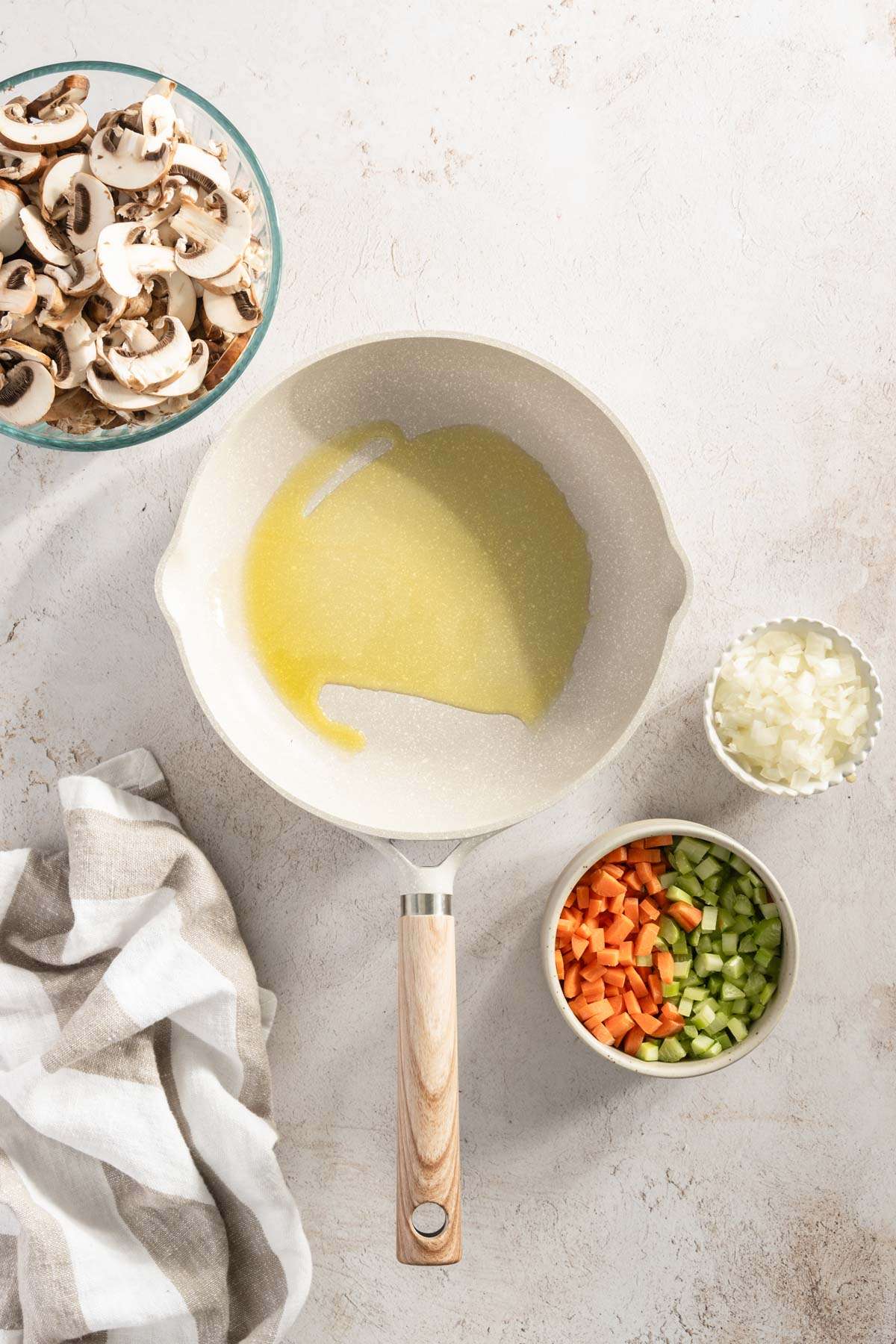 frying pan with drizzle of oil, small bowl with chopped onions; small bowl with sliced mushrooms and another one with carrots and celery