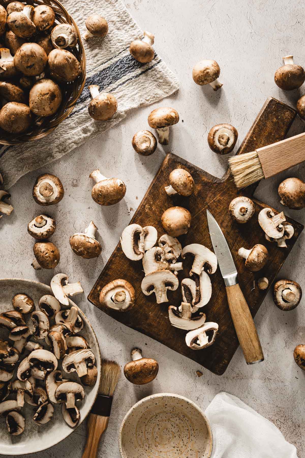 mushrooms scattered on the table, some in a basket, some on a cuttings board