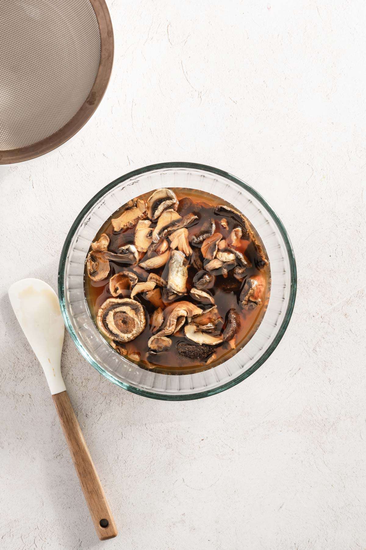 rehydrated mushrooms in a bowl, spatula and strainer on the side