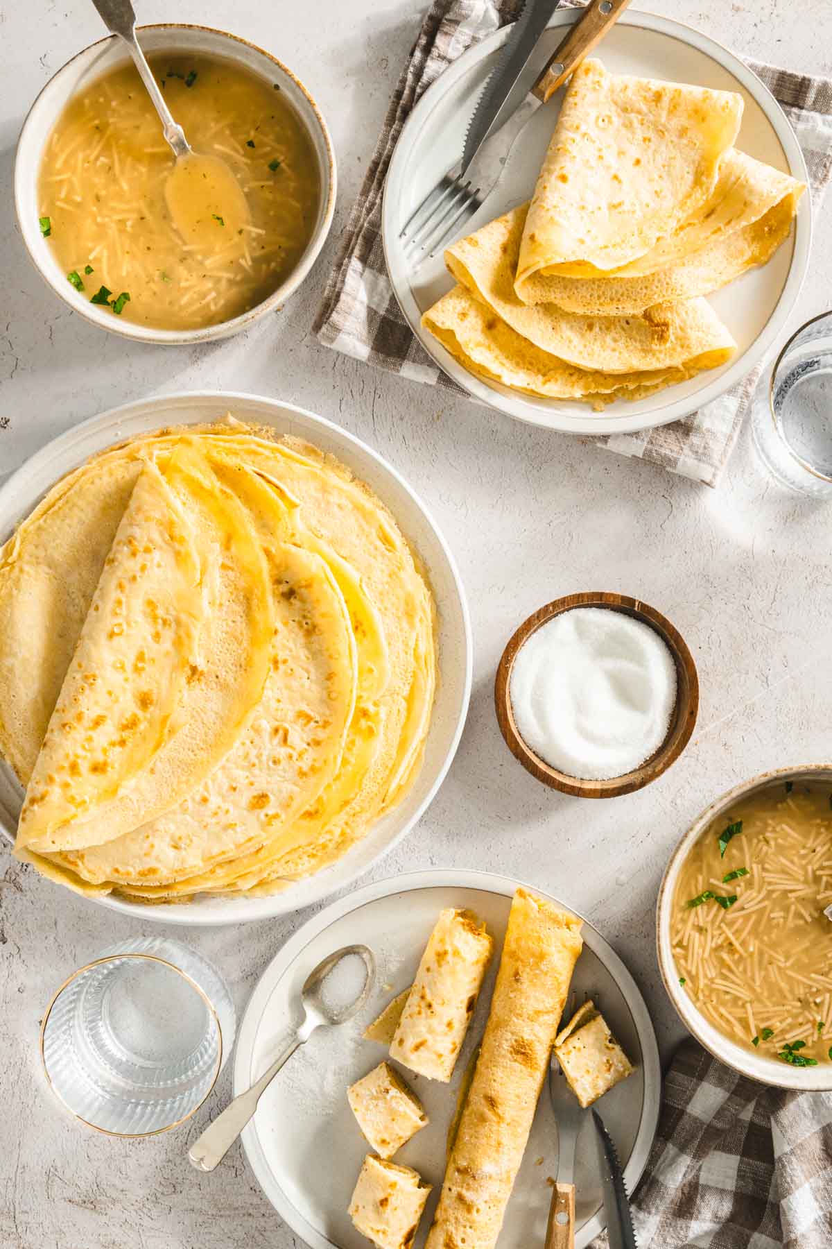 various plates with nalesniki folded in different ways. two bowls with chicken soup, dish with sour cream